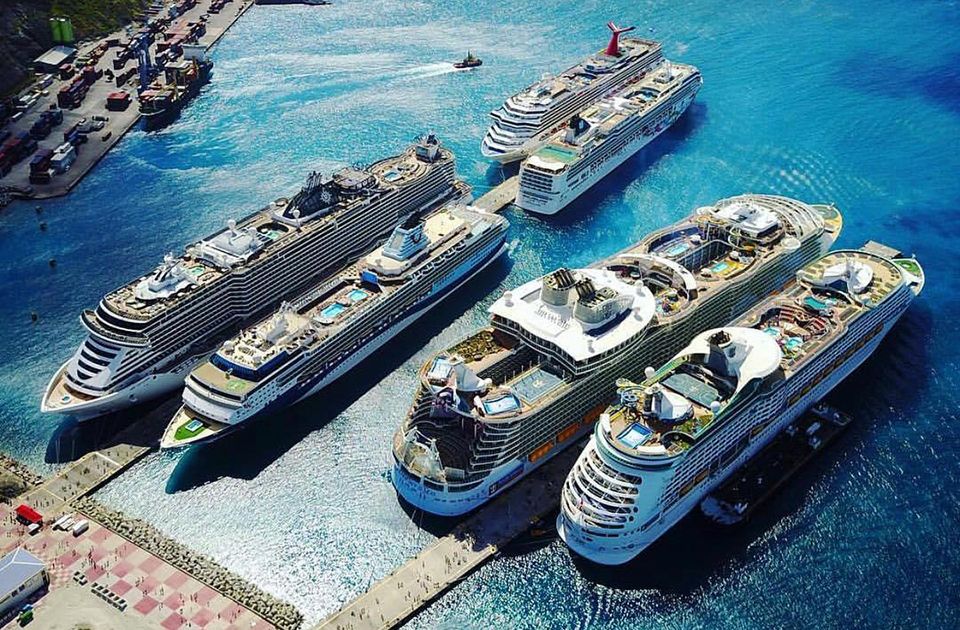 Aerial view of multiple large cruise ships docked at a Caribbean port with turquoise waters.