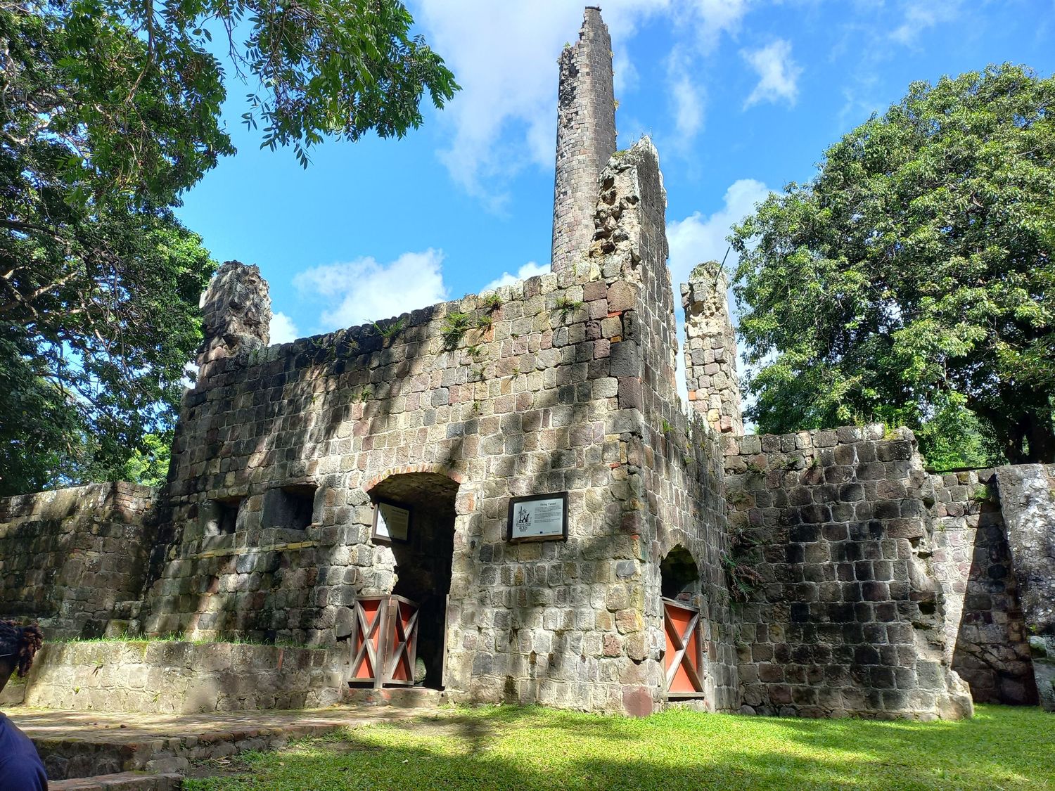 Ancient stone ruins with a tall tower surrounded by lush green trees under a bright blue sky.