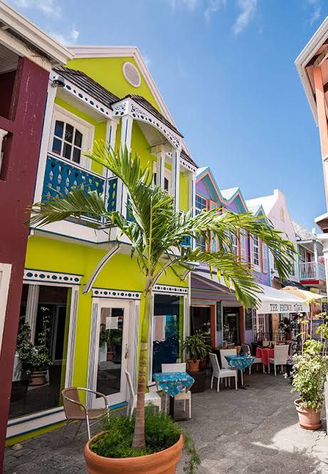 Colorful vibrant Caribbean shopping street with lime green buildings, balconies, and palm trees in a tropical setting.