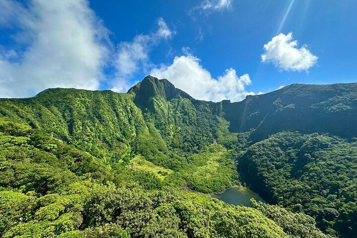 Lush green mountains with dramatic peaks under a blue sky with white clouds in a tropical Hawaiian landscape.