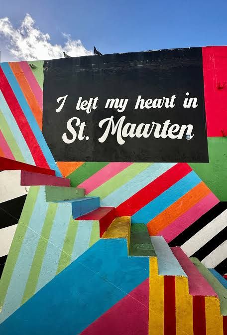 Colorful striped mural with black sign reading I left my heart in St. Maarten on a vibrant painted wall.