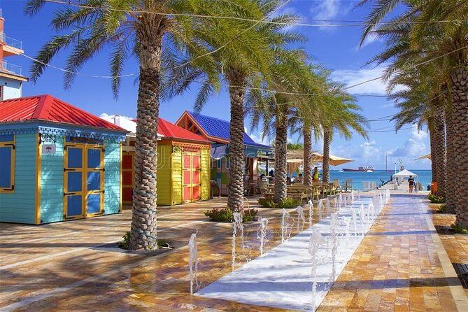 Colorful Caribbean waterfront shops with palm trees and clear blue skies on a sunny tropical promenade.