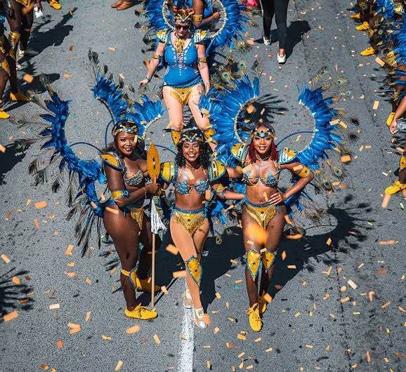 Vibrant carnival dancers in blue and yellow feathered costumes parade through streets with confetti falling around them.