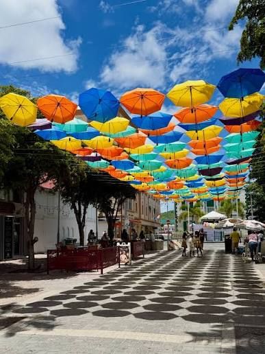 Colorful open umbrellas suspended over a checkered pedestrian street on a sunny day.