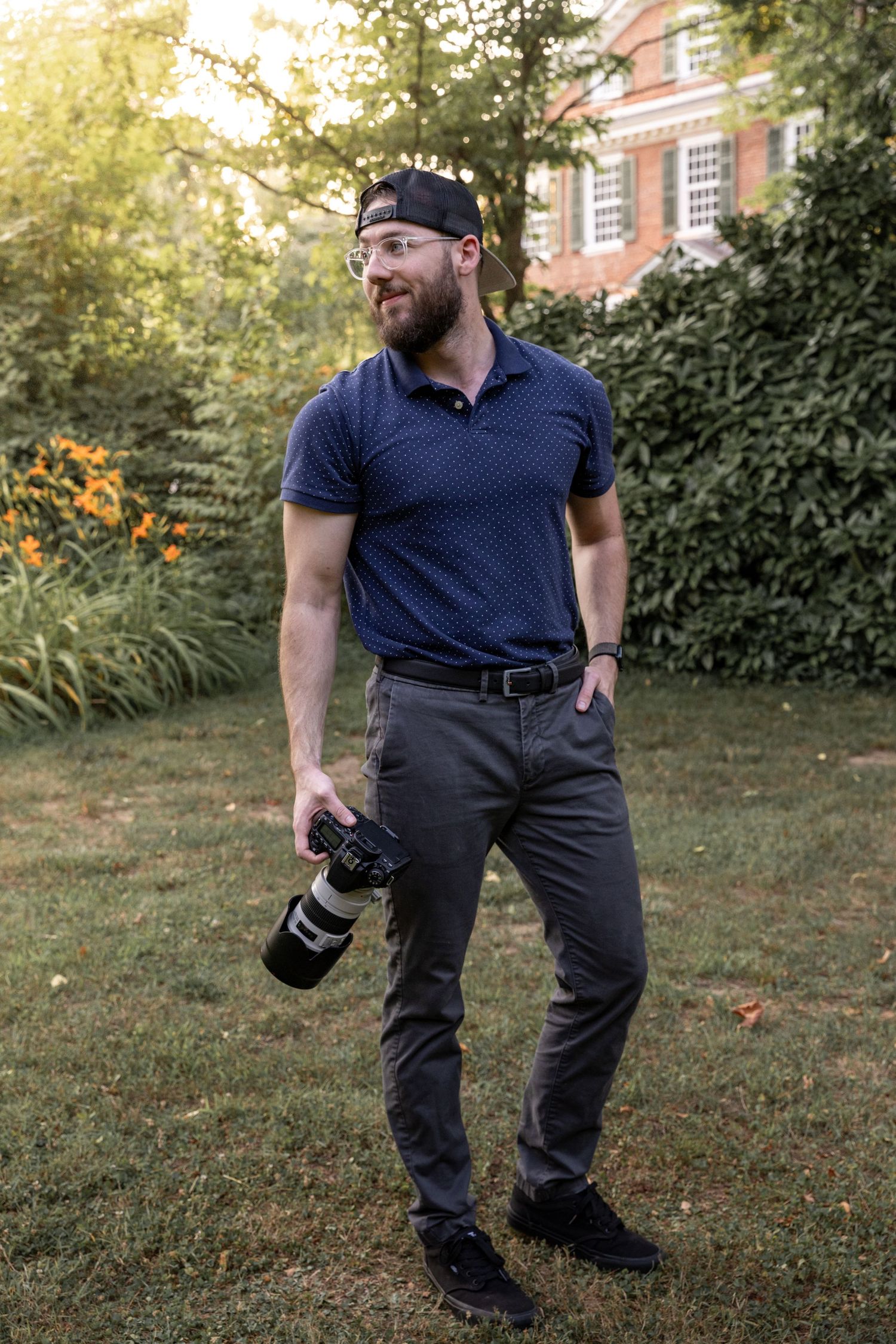 Professional photographer in navy polo holding camera while working outdoors.