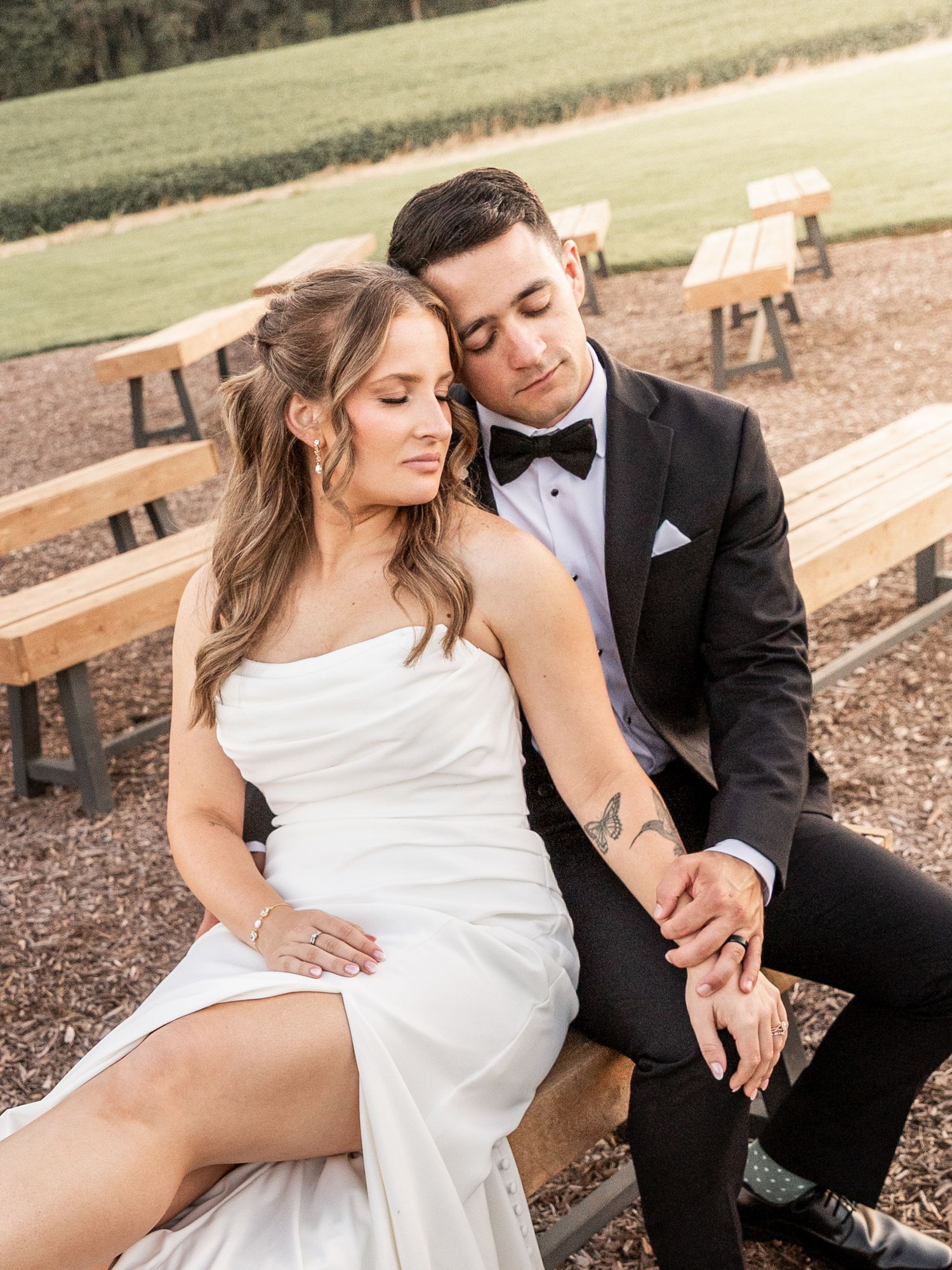 A bride and groom share a romantic moment seated on a wooden bench outdoors at their elegant wedding celebration.