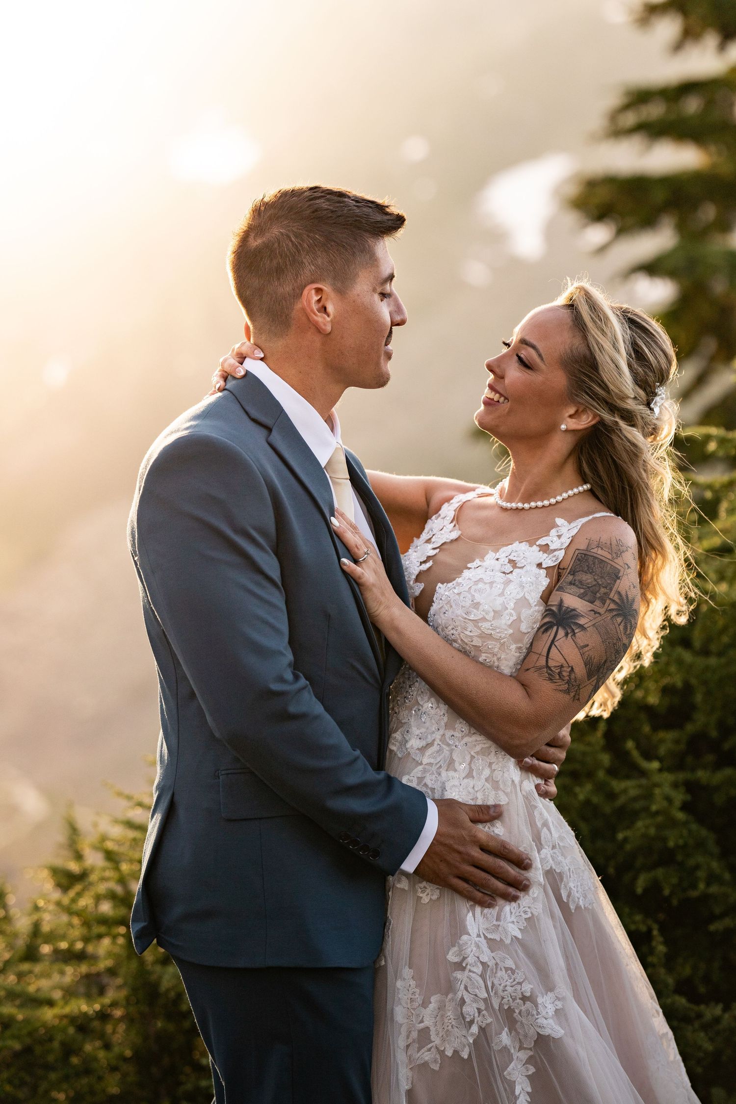 A bride and groom embrace in a romantic outdoor sunset moment wearing traditional wedding attire.
