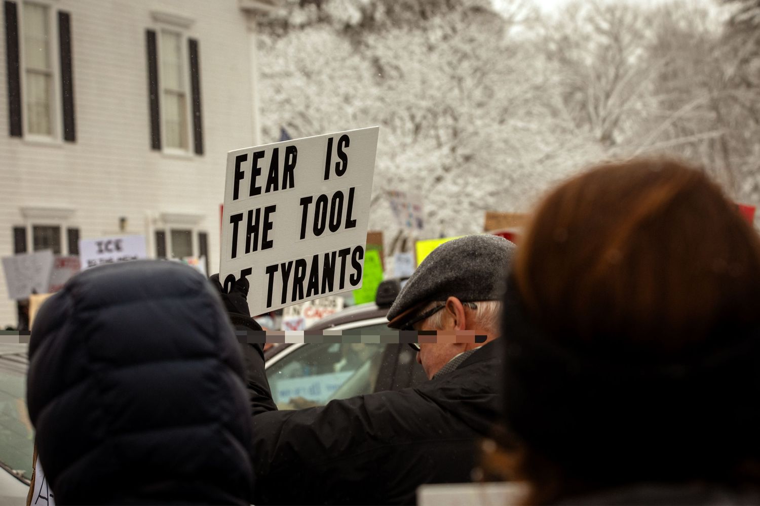 Person amongst a crowd, holding a sign that reads, 
