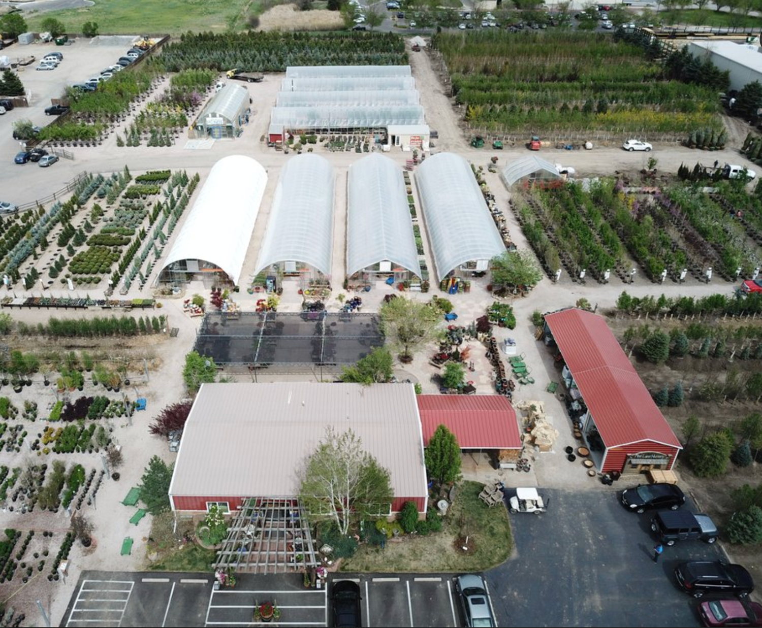 Aerial view of a large garden nursery with greenhouses, plant rows, red barn buildings, and parking lot.