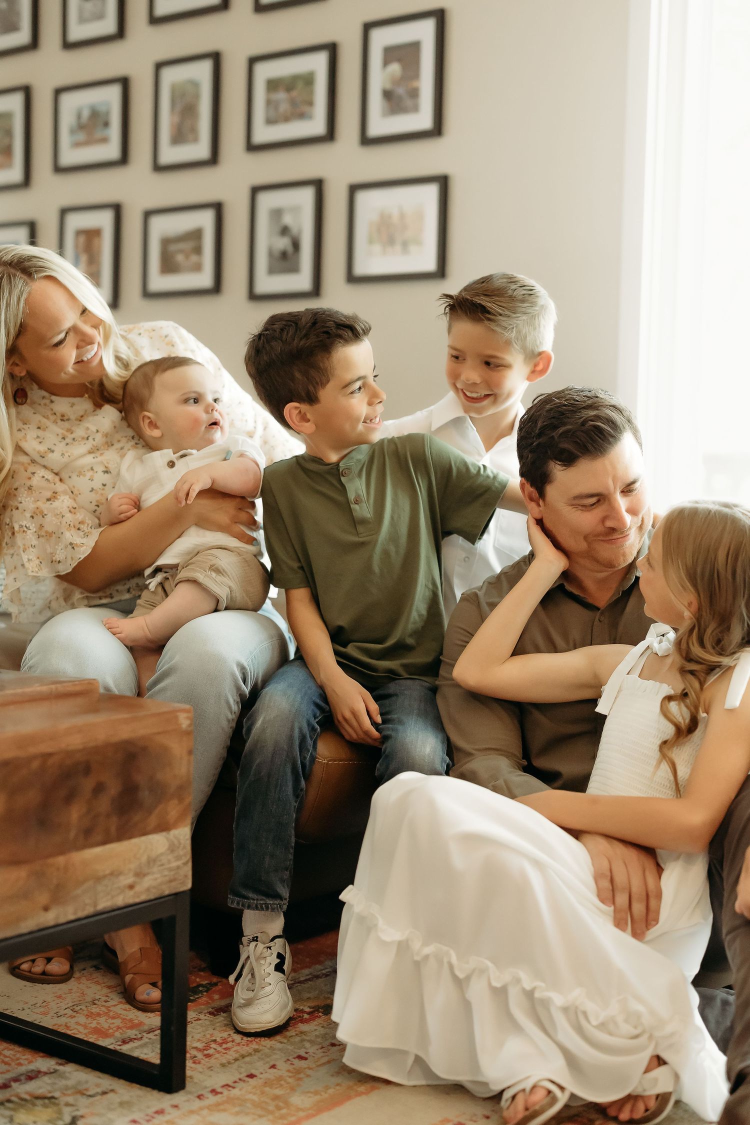 Family gathering on couch in living room with gallery wall of framed artwork.