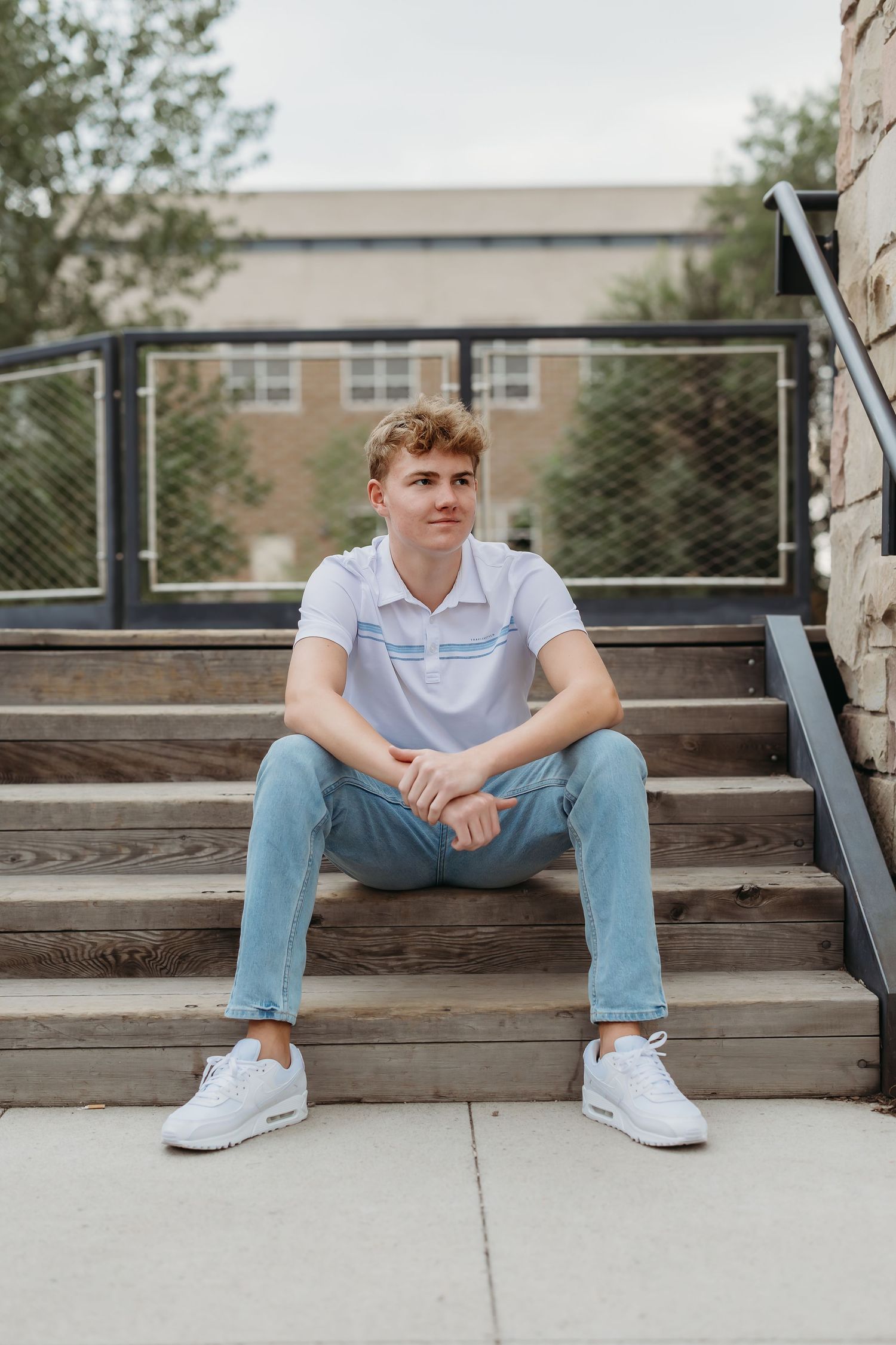 Relaxed outdoor portrait on wooden bleachers wearing polo shirt and light jeans.