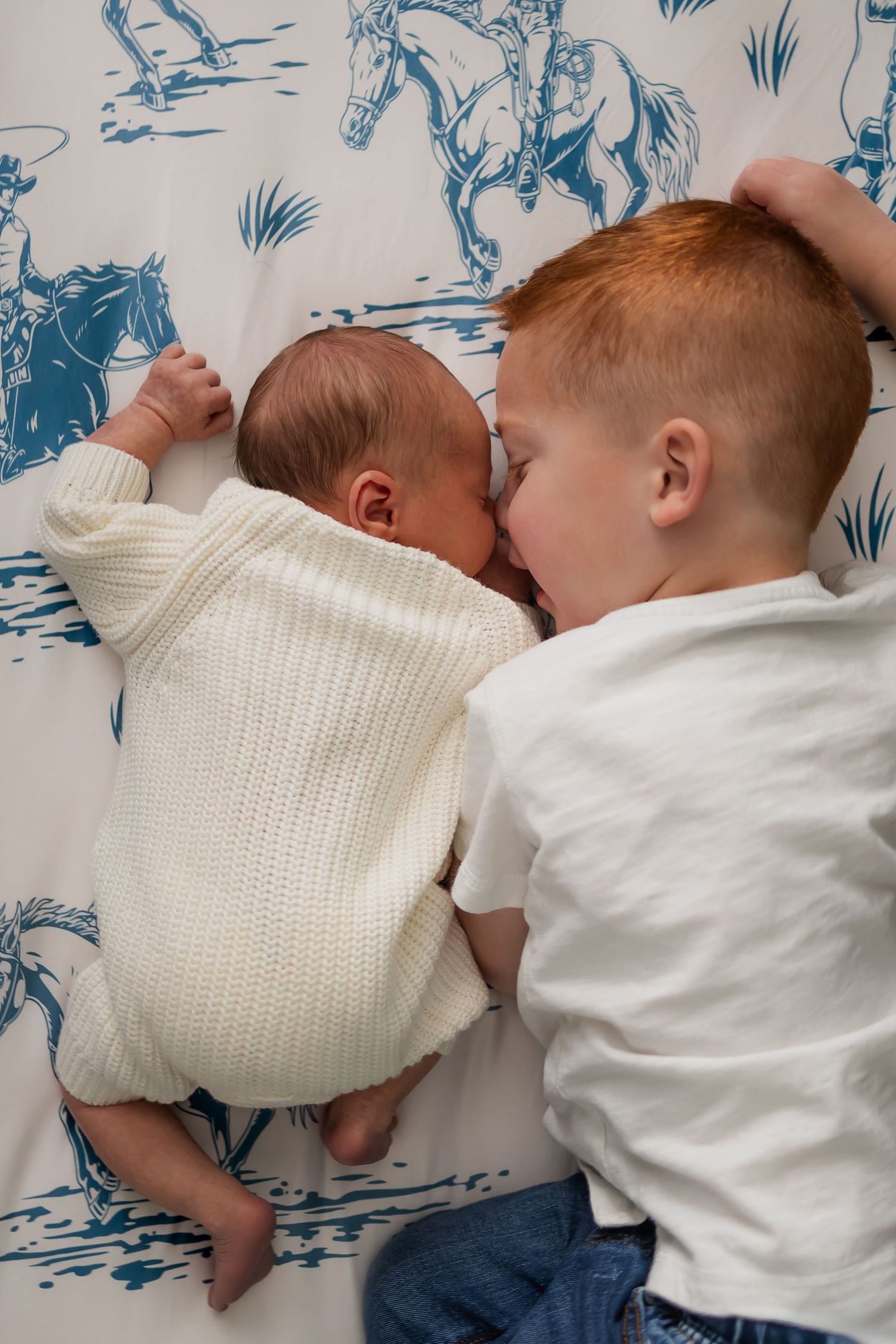 Two babies lying side by side on blue and white patterned bedding.