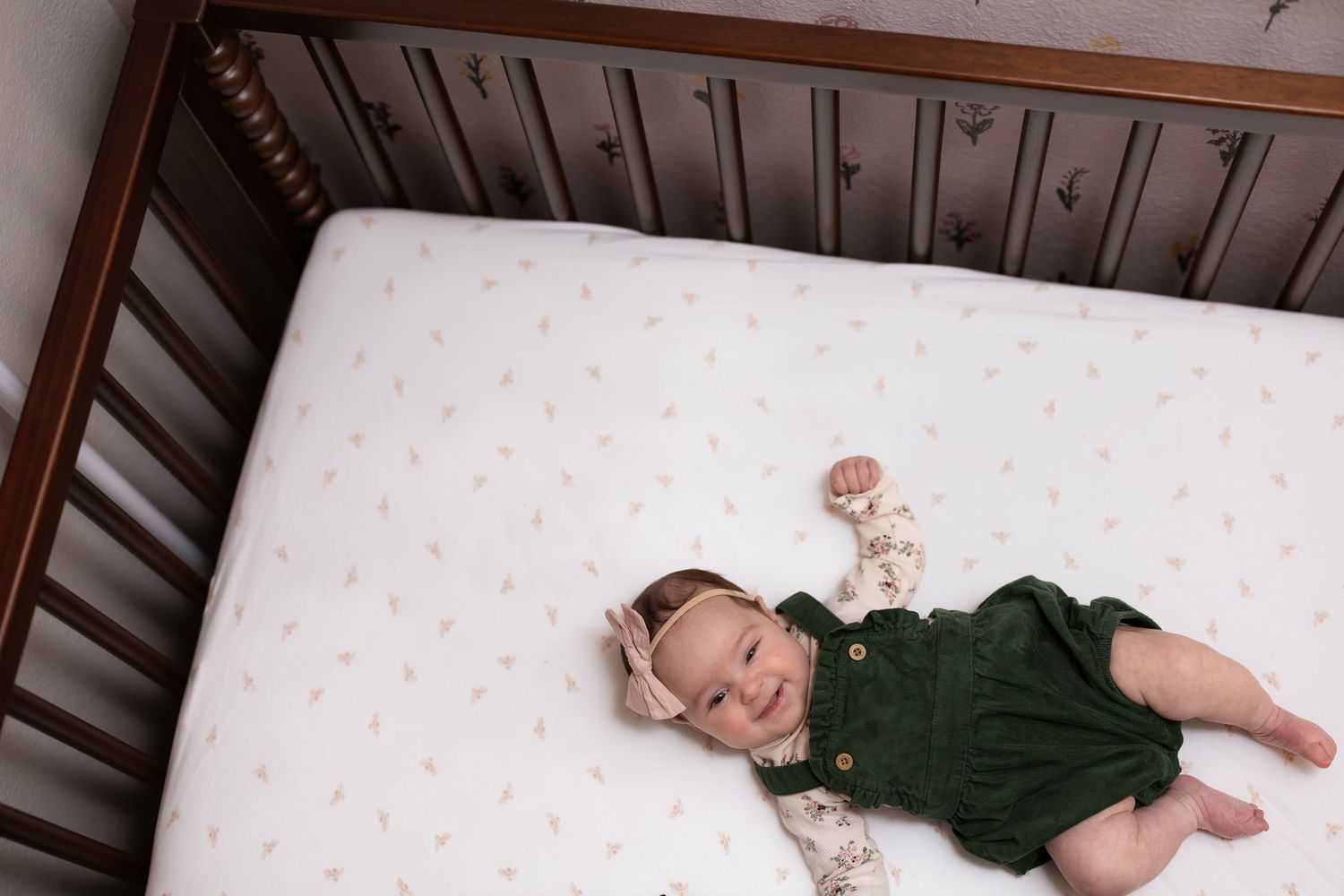 Baby resting on floral patterned background wearing dark green outfit.