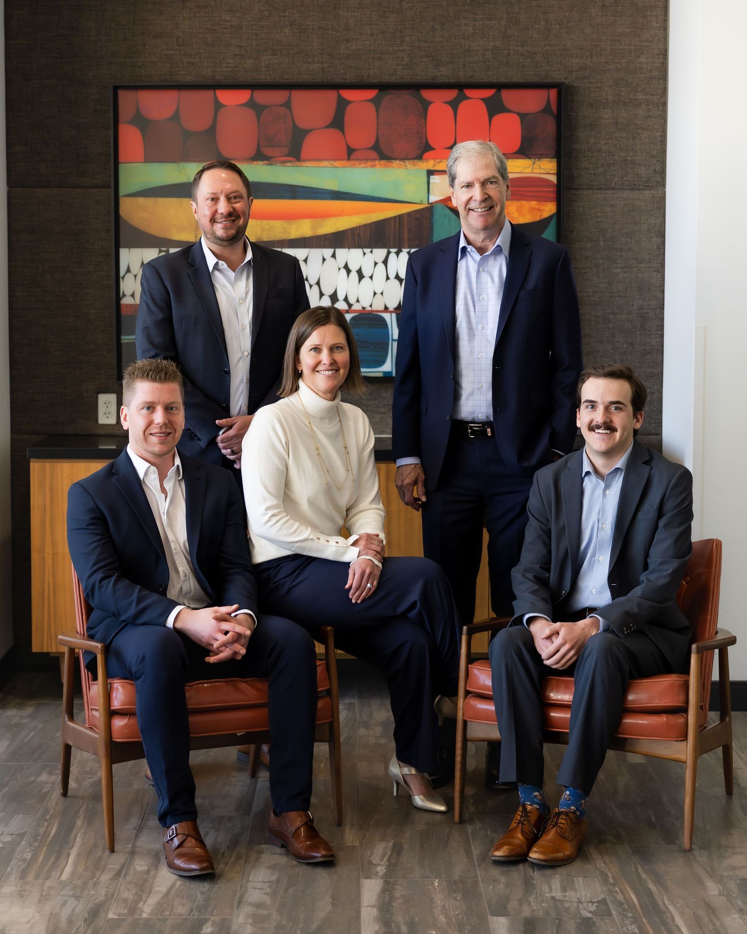 Business team seated on vintage chairs against dark wall with modern artwork.