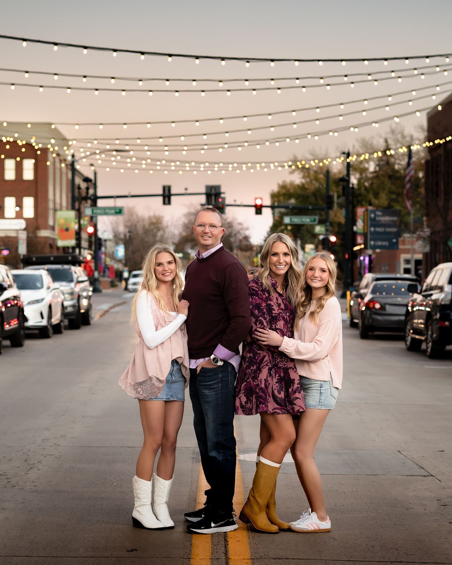 Family posing under string lights in an urban setting at dusk.