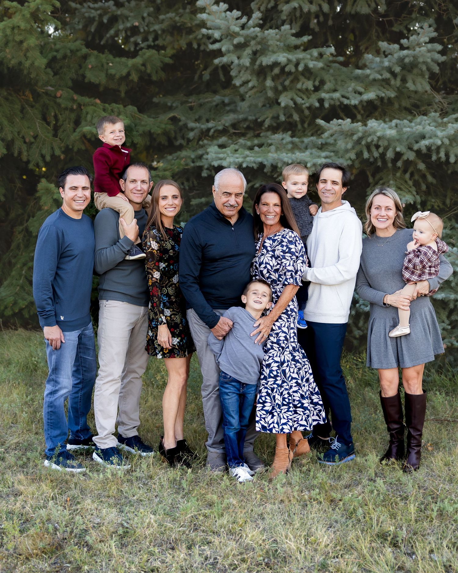 Extended family gathering for a group photo in front of evergreen trees.