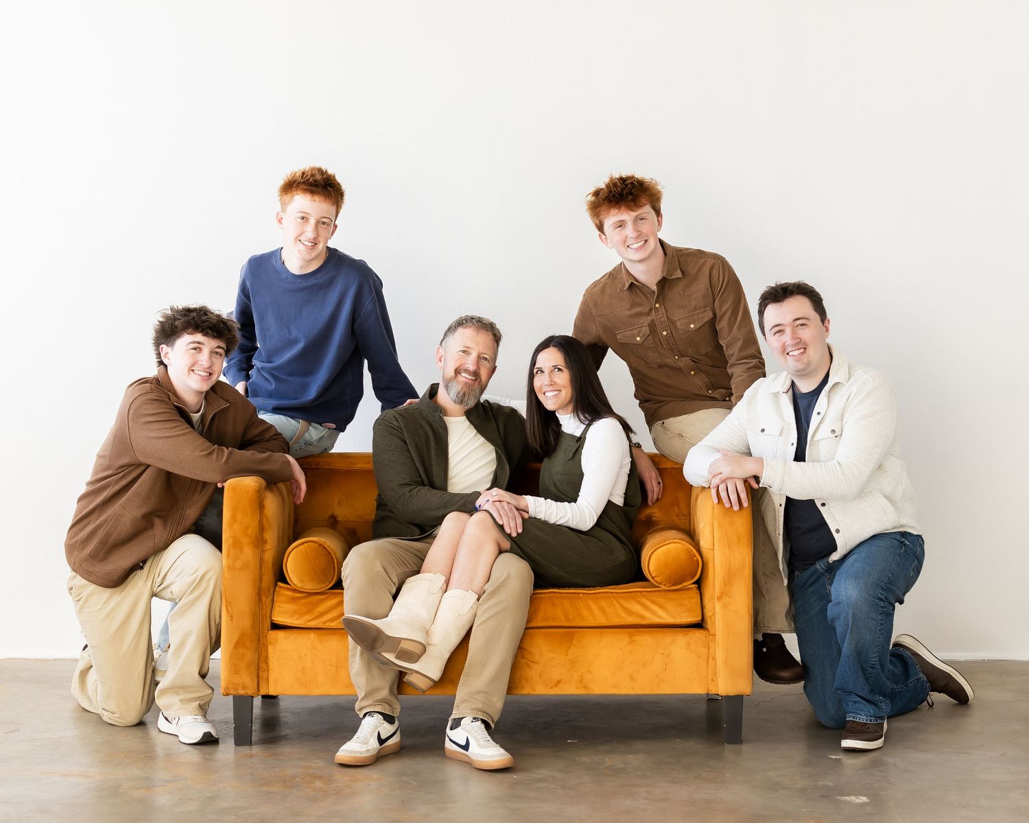 Group of people lounging together on an orange couch against white wall.