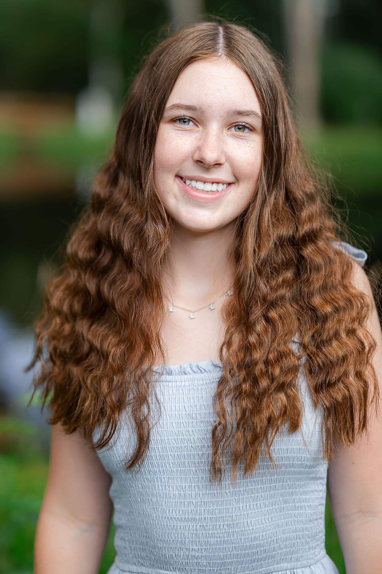 Portrait with long curly hair against blurred green background.