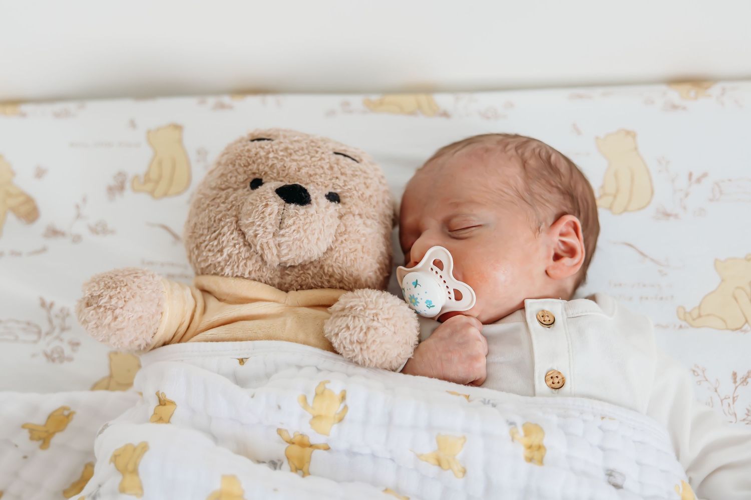 Newborn baby sleeping peacefully on white and gold patterned bedding.