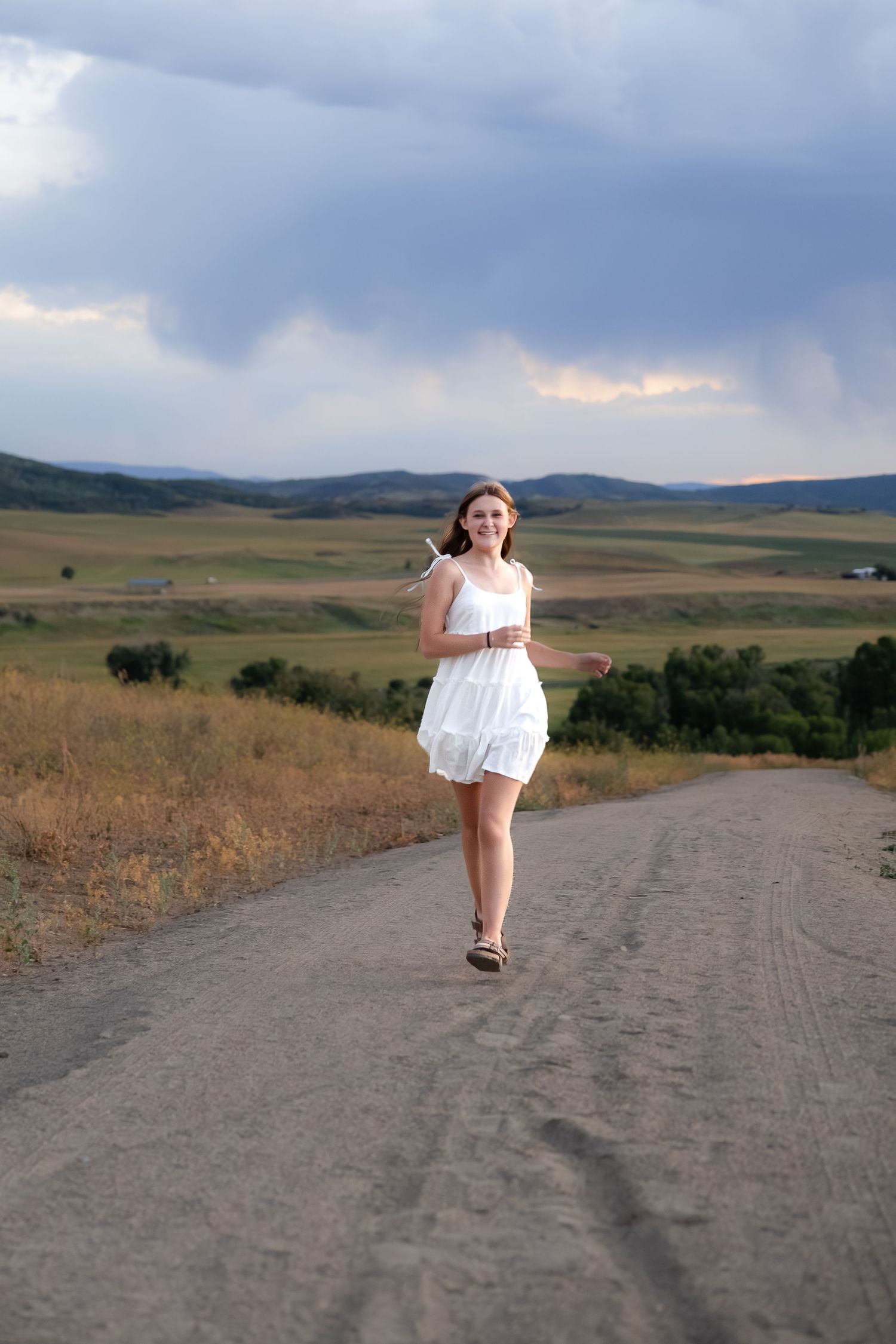 White summer dress on dirt road with dramatic stormy sky and rolling hills.