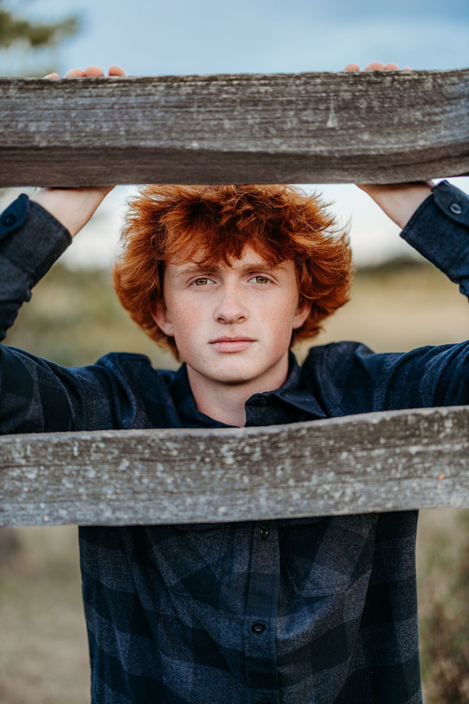 Person in dark shirt peering through wooden fence slats during outdoor portrait session.