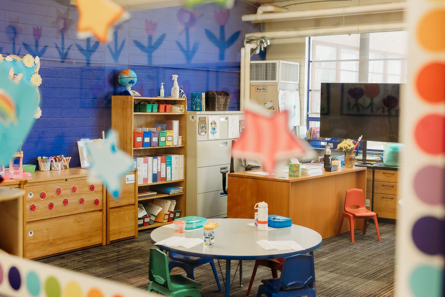 Colorful classroom interior with blue walls, wooden furniture and playful decor.