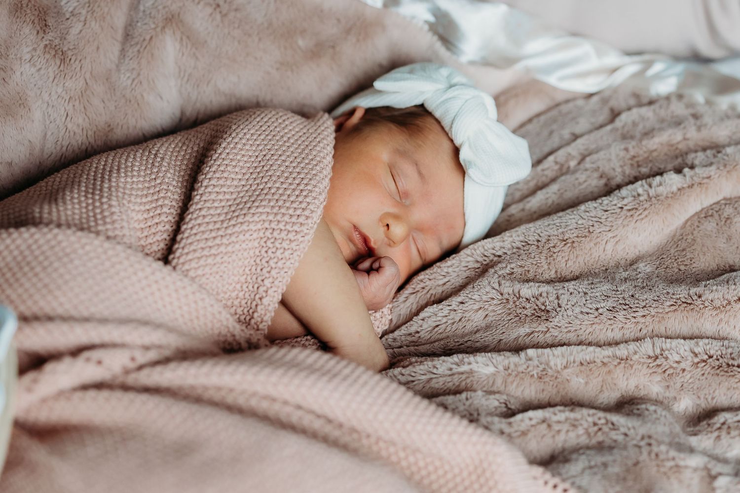 Newborn baby sleeping peacefully on soft beige blankets.