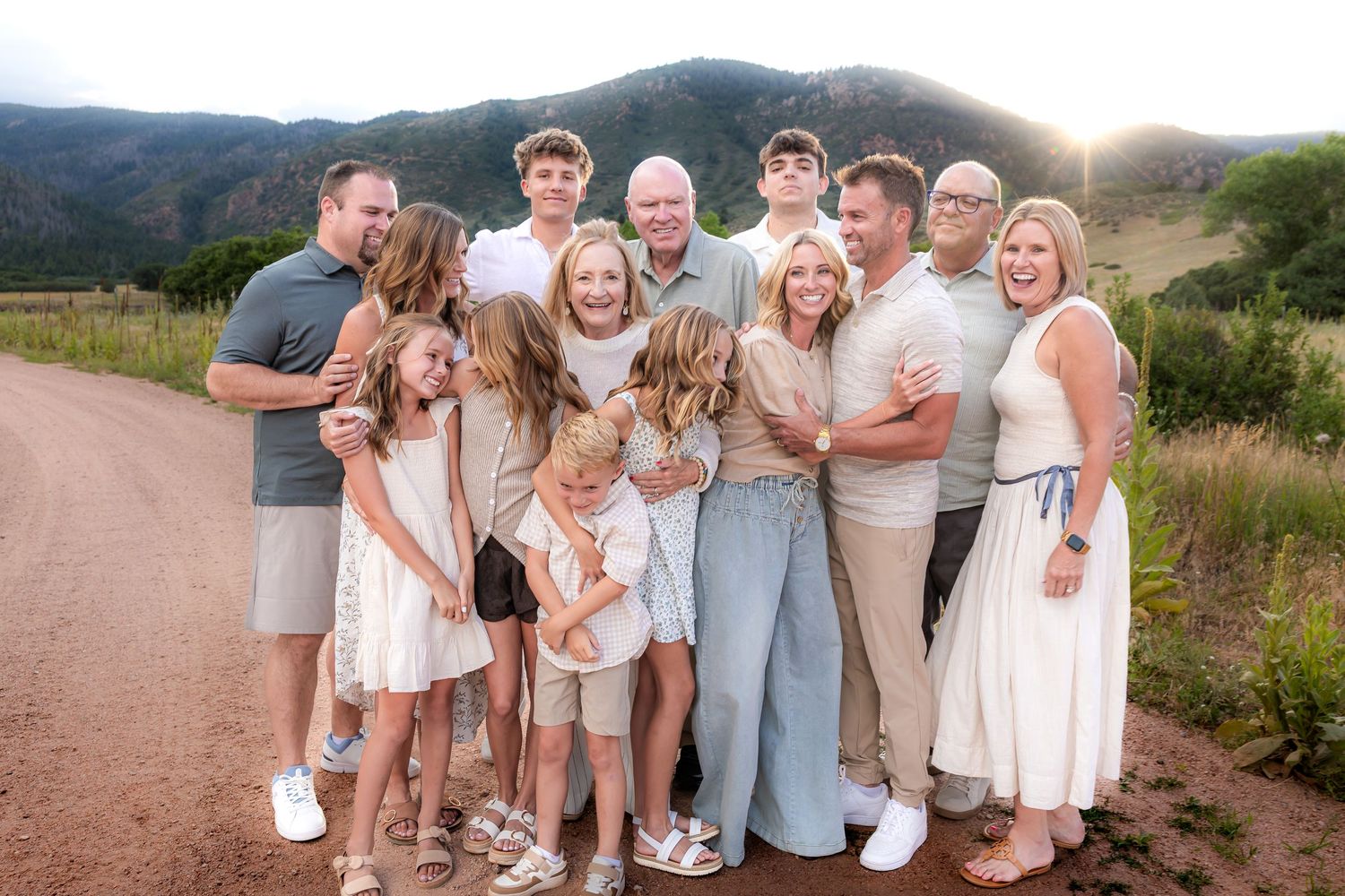 A multi-generational family group poses together on a dirt path with scenic mountain views in the background.