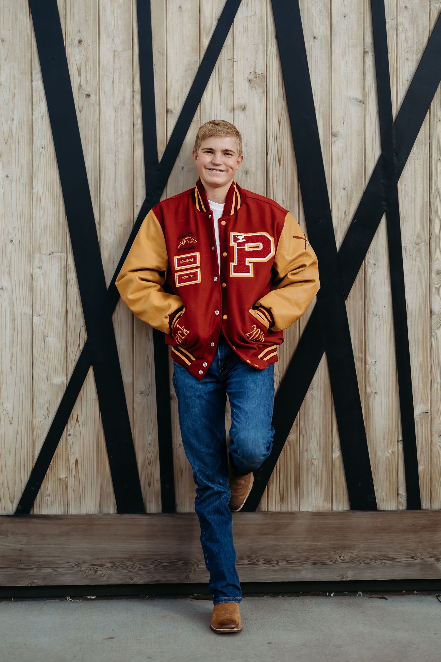 Varsity letterman jacket pose against geometric wooden wall pattern.