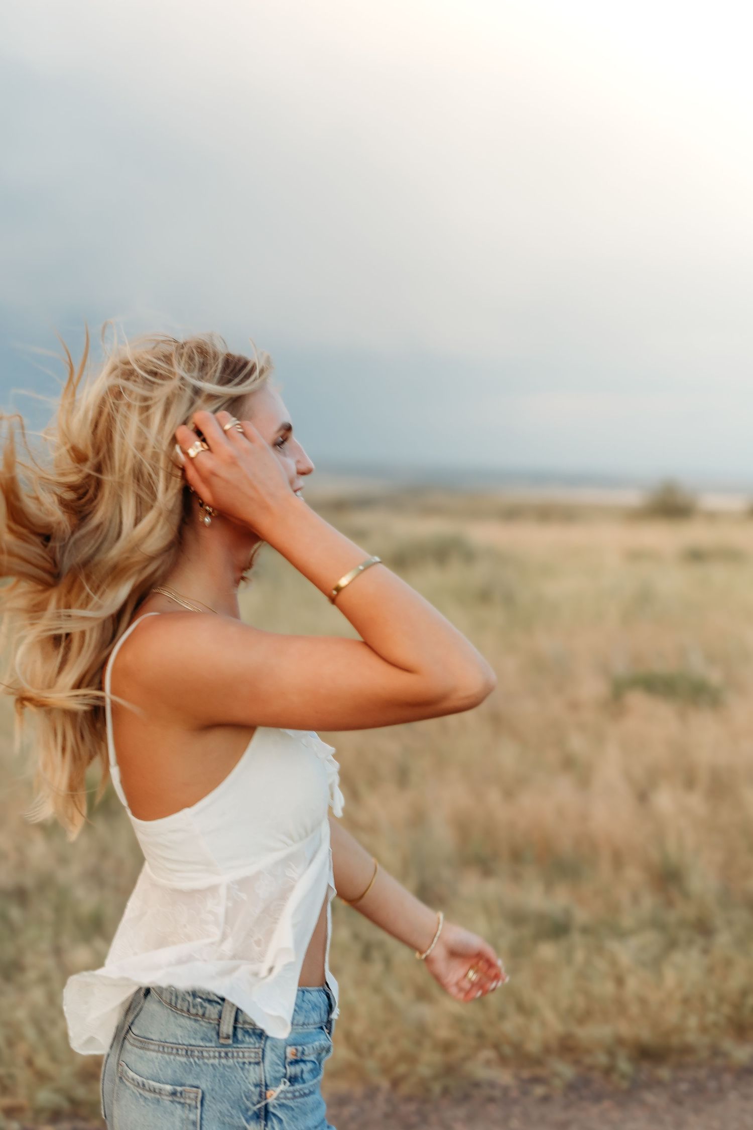 Woman in white tank top and denim enjoying carefree moment in golden field.