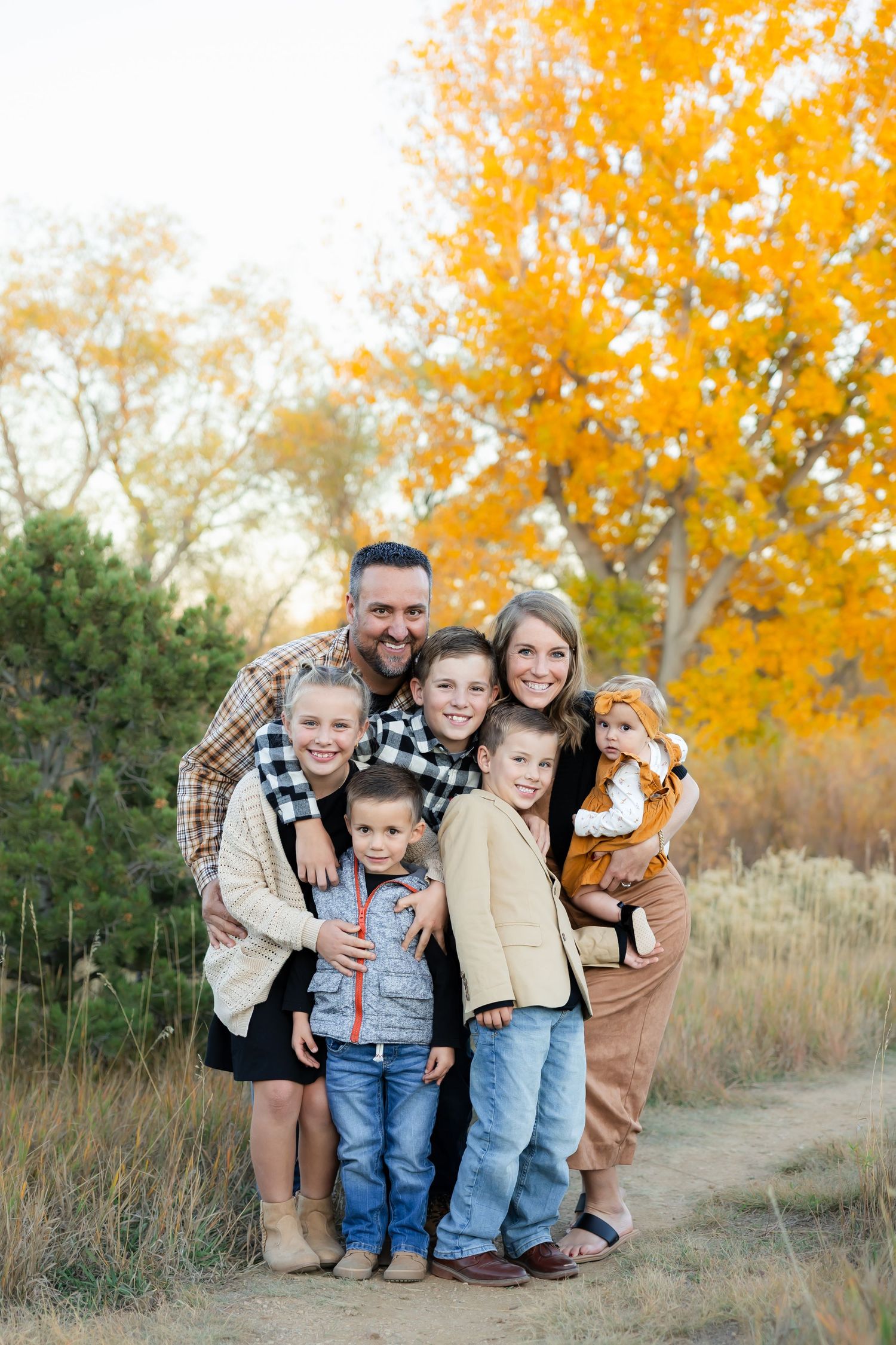 Family portrait session outdoors with vibrant fall foliage and golden leaves in the background.