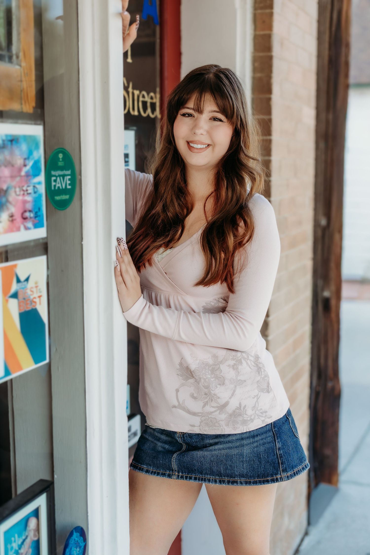 Woman in white long sleeve top posing playfully against storefront windows.
