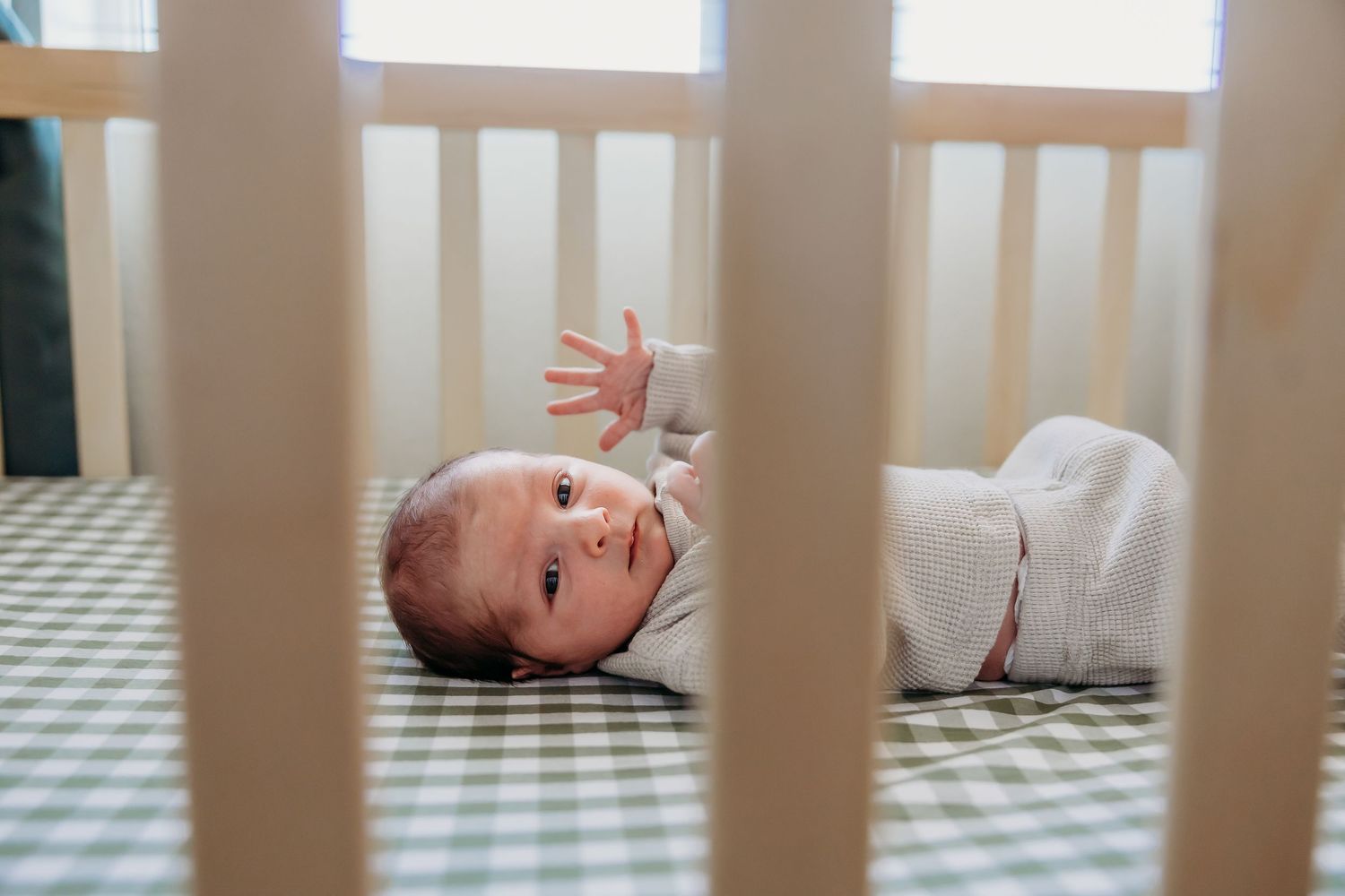 Baby lying in white crib with sunlight streaming through windows.