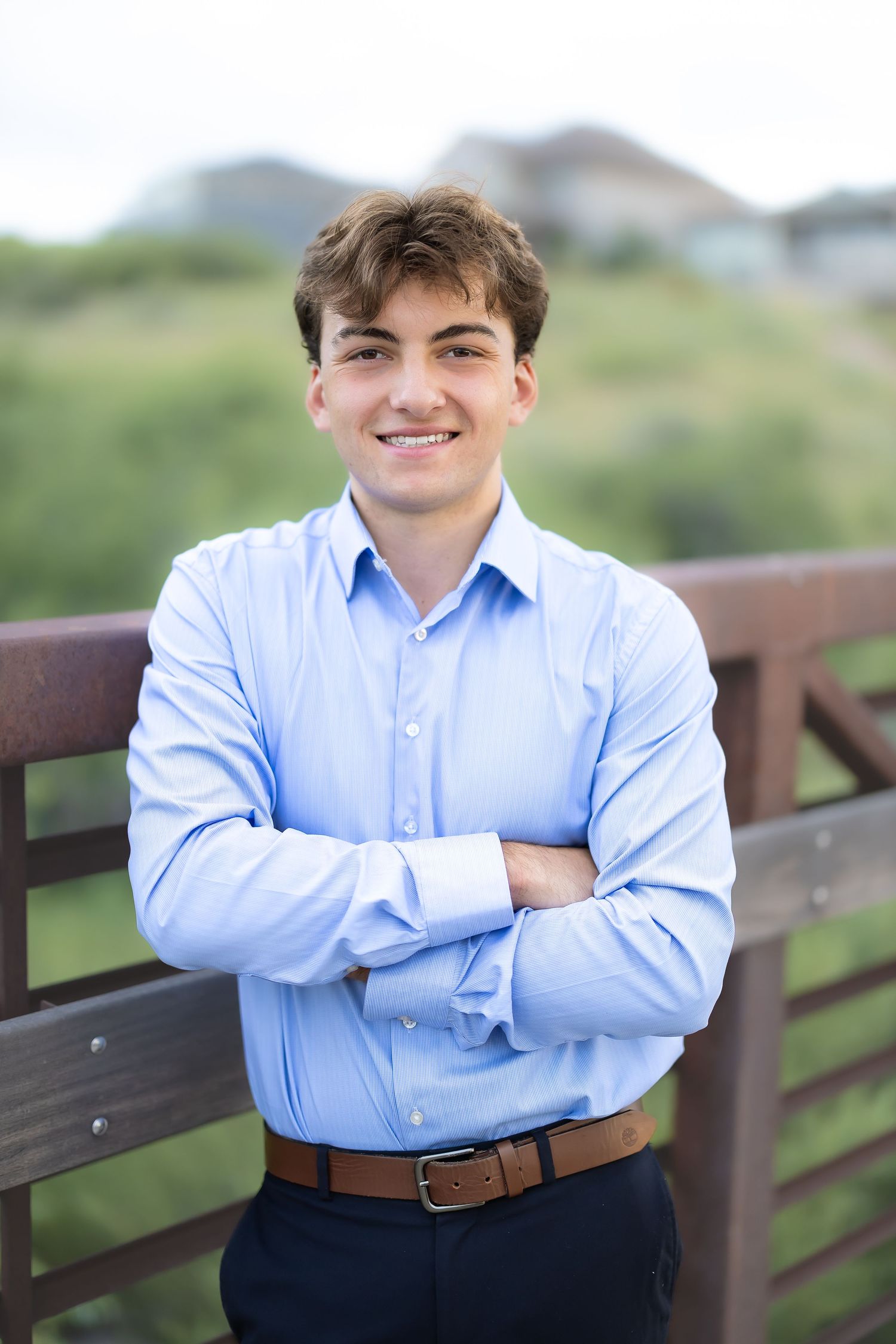 Person in light blue dress shirt and dark pants posing against wooden railing.