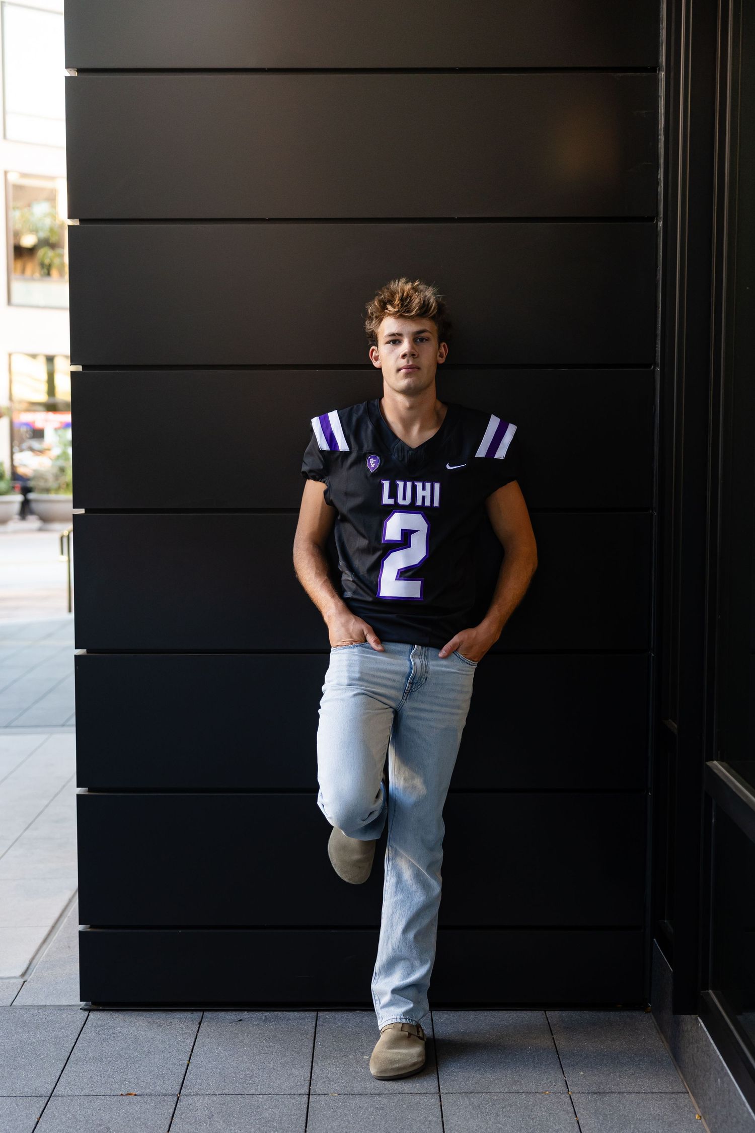 Athletic figure poses against black wall wearing blue football jersey number 2.