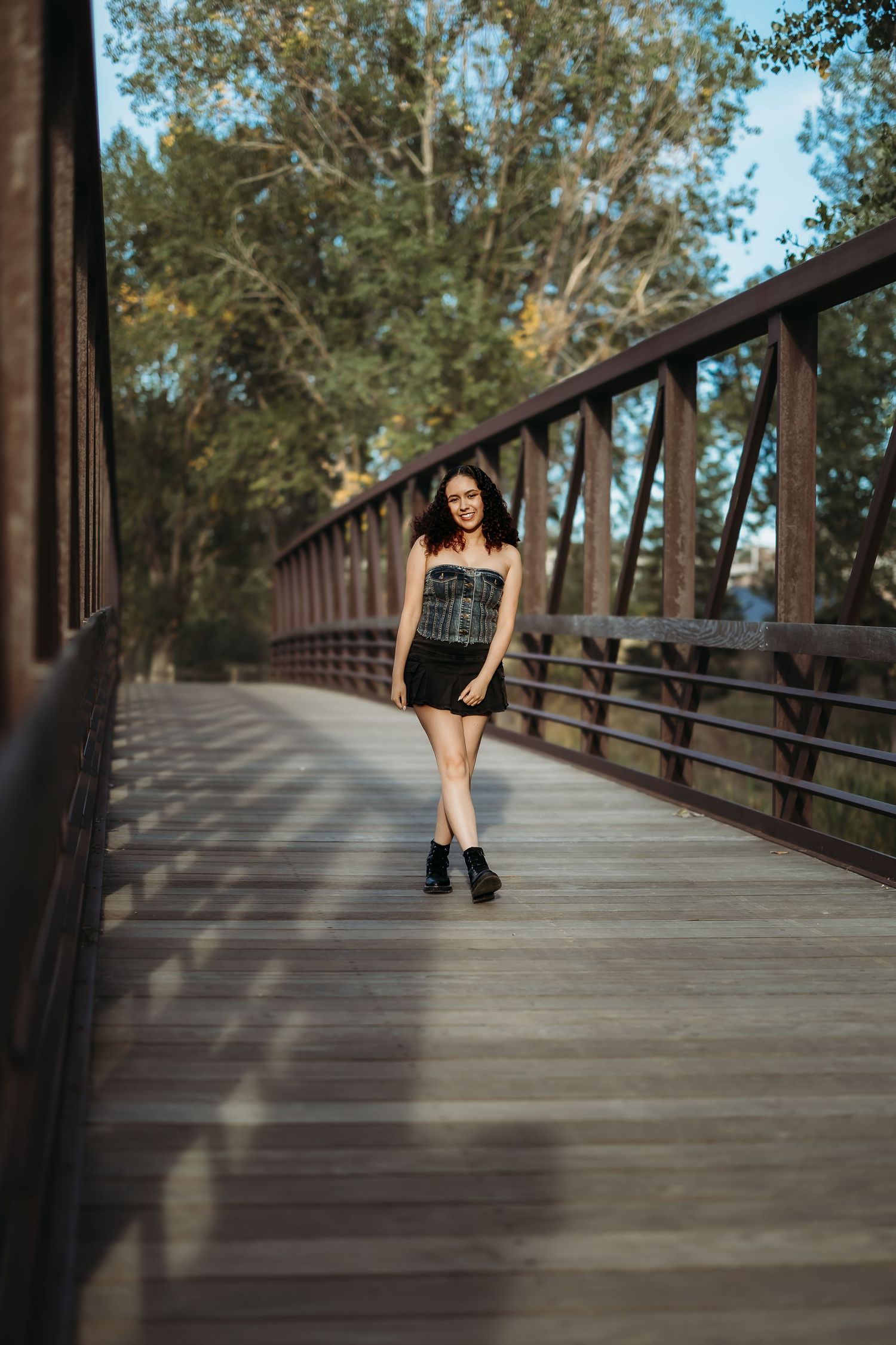 Wooden boardwalk through trees with person in black outfit sitting in distance.