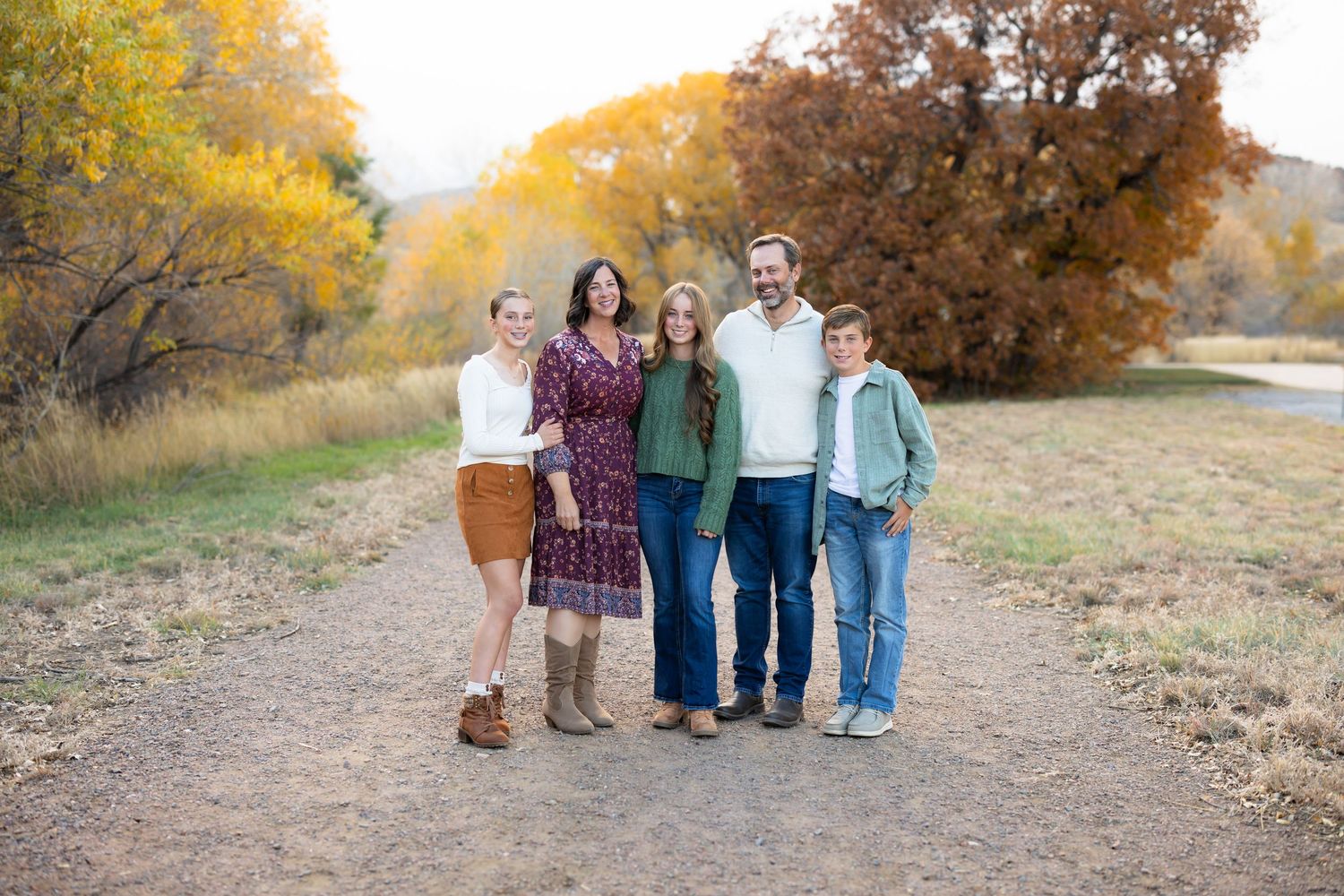 A group of people walking on an autumn trail with golden trees and foliage in the background.