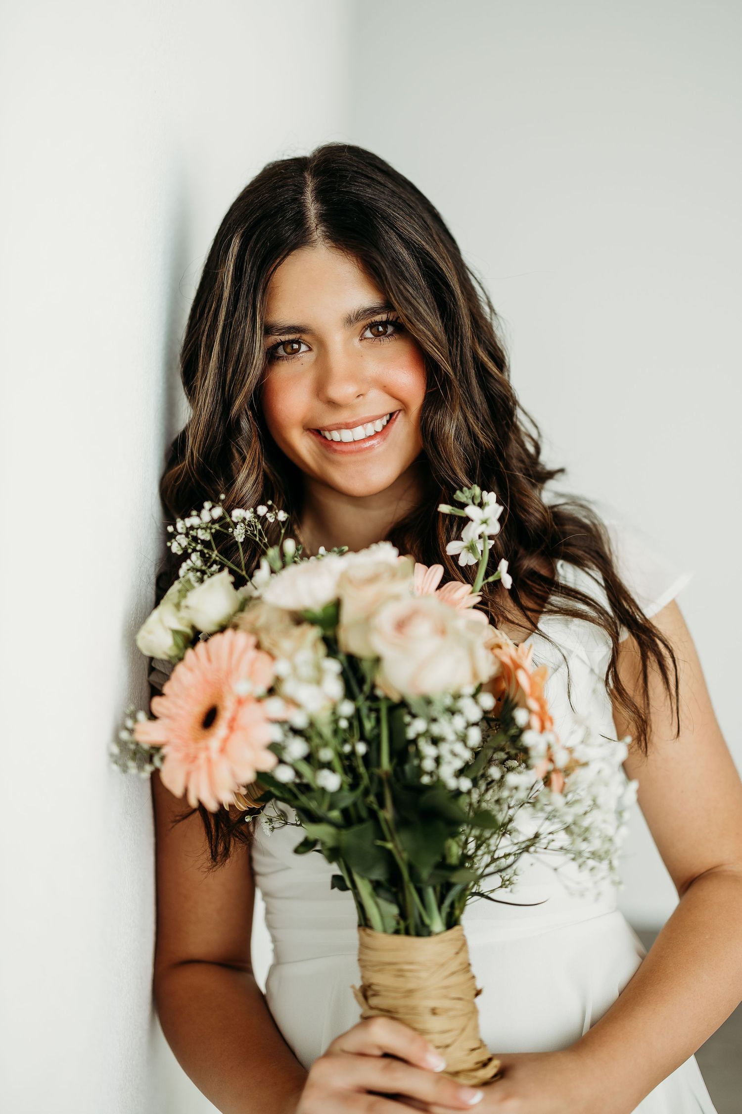 8th grade girl in white holding a bouquet of pink gerbera daisies and baby's breath flowers.