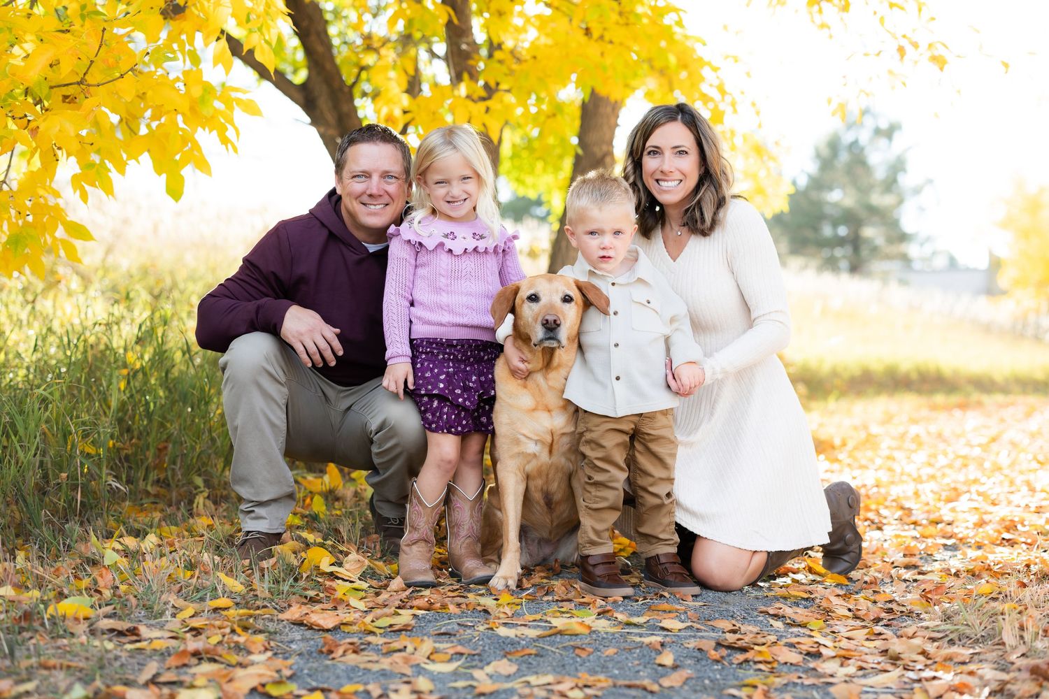 Family photo session with golden autumn leaves and natural outdoor backdrop.