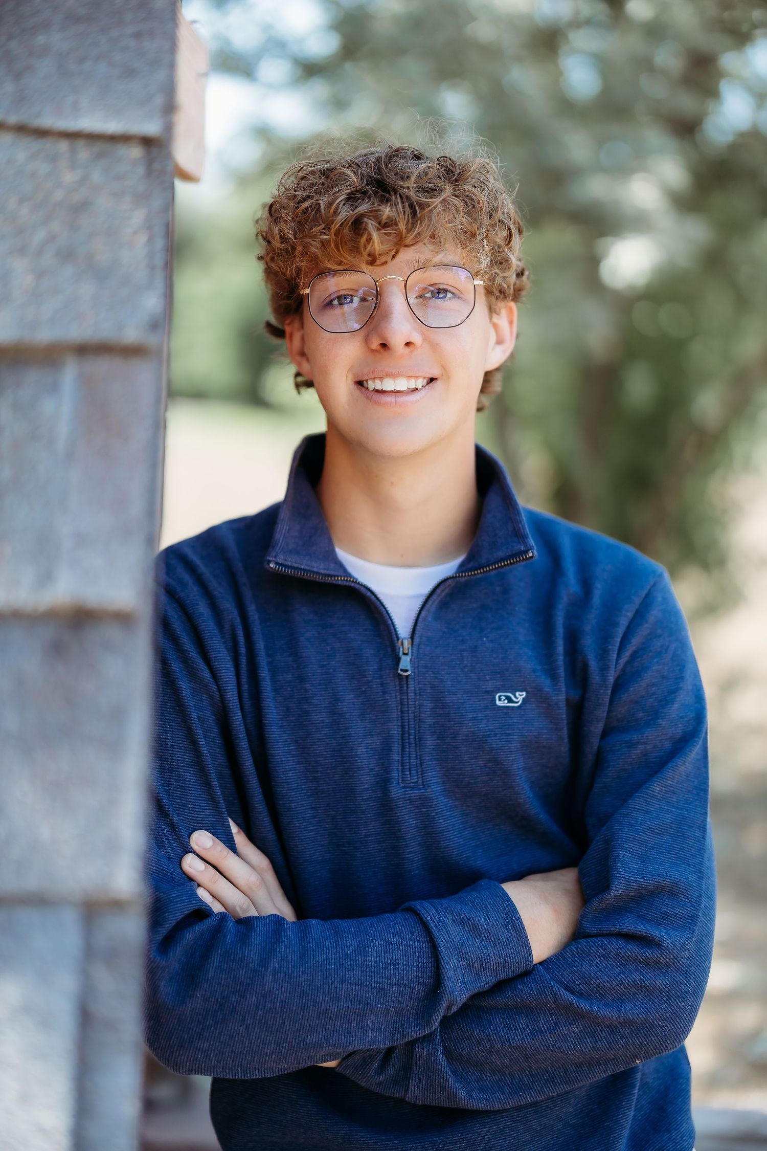 Portrait of someone in navy blue quarter-zip sweater and glasses against outdoor background.