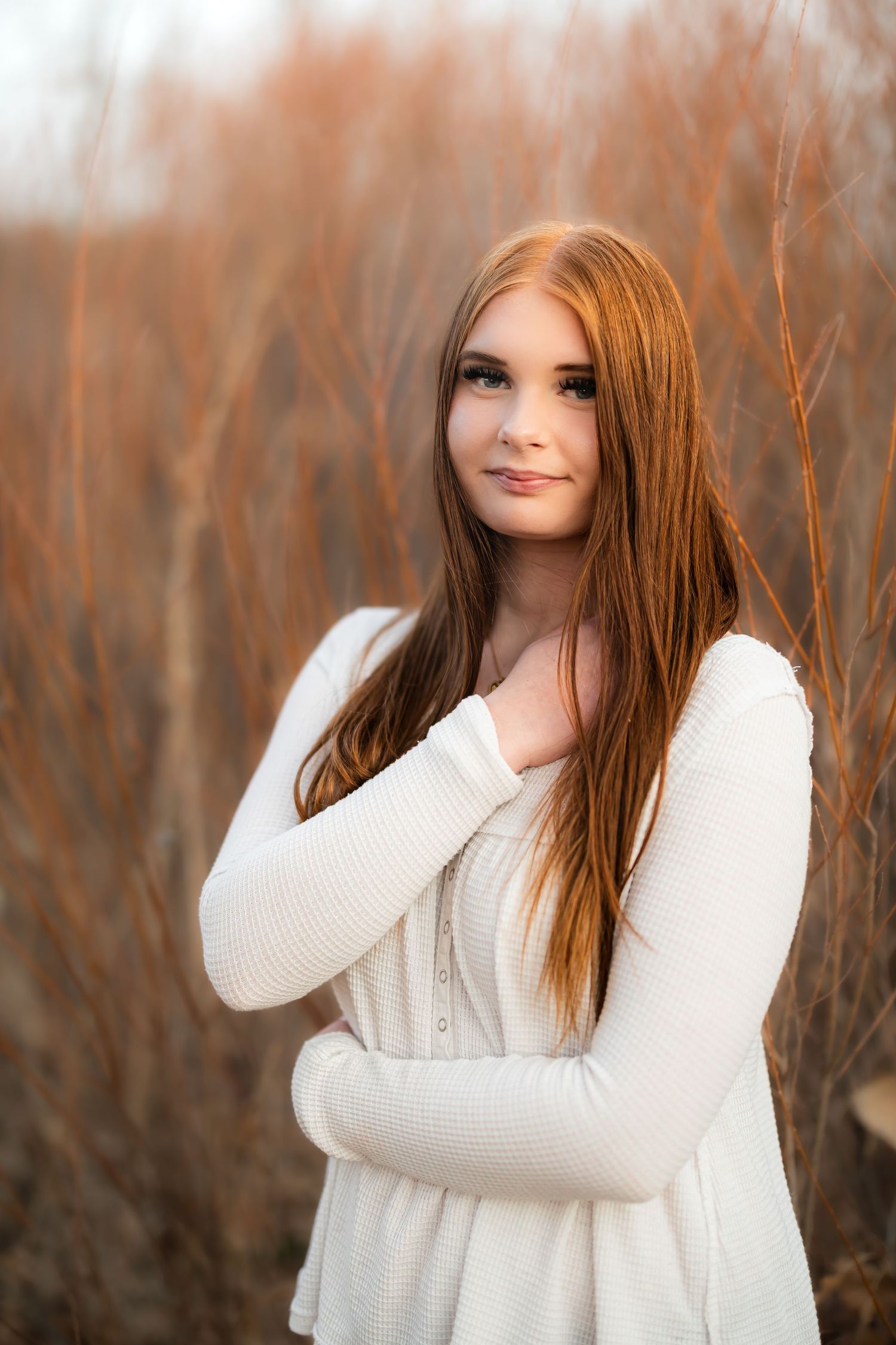 Portrait of a woman in a white sweater posing outdoors against a blurred autumn background.