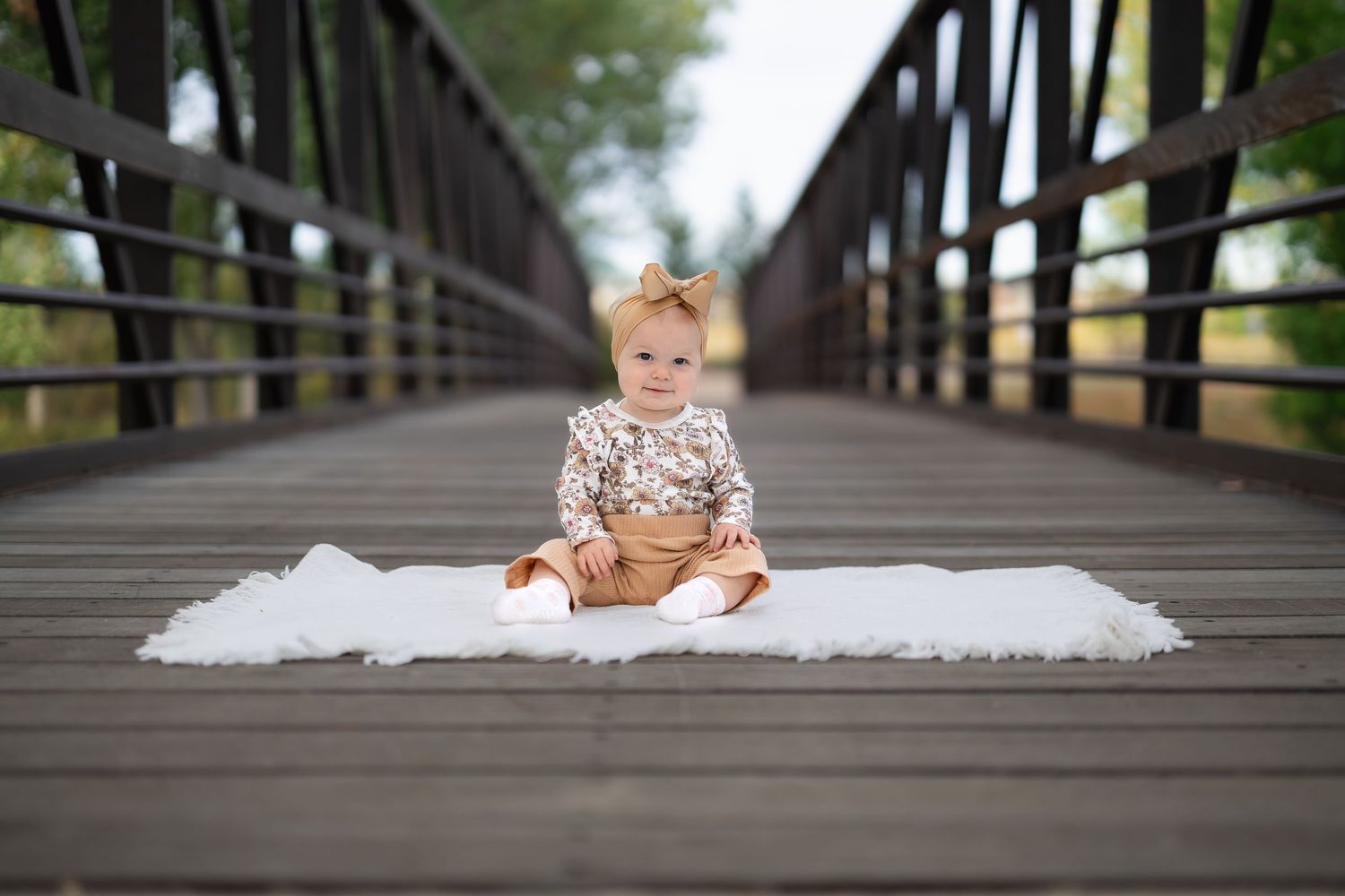 Baby sitting on wooden bridge outdoors with white fabric.
