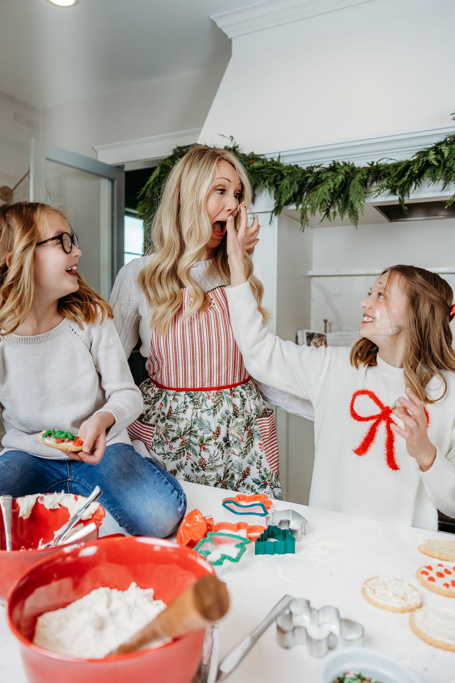 Holiday cookie decorating scene with festive garland and baking supplies in a bright kitchen.