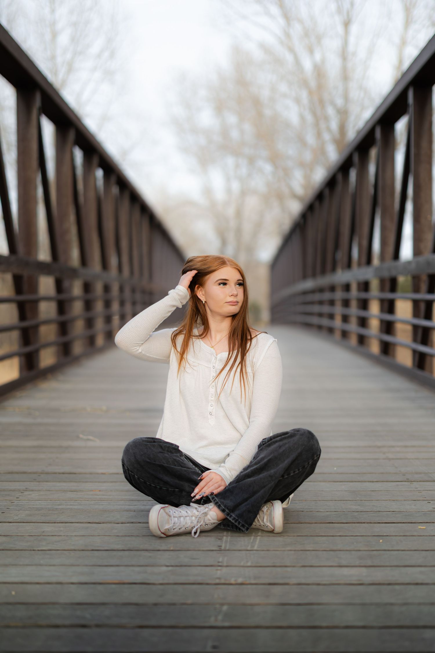 Person in white sweater sitting cross-legged on a wooden bridge walkway.