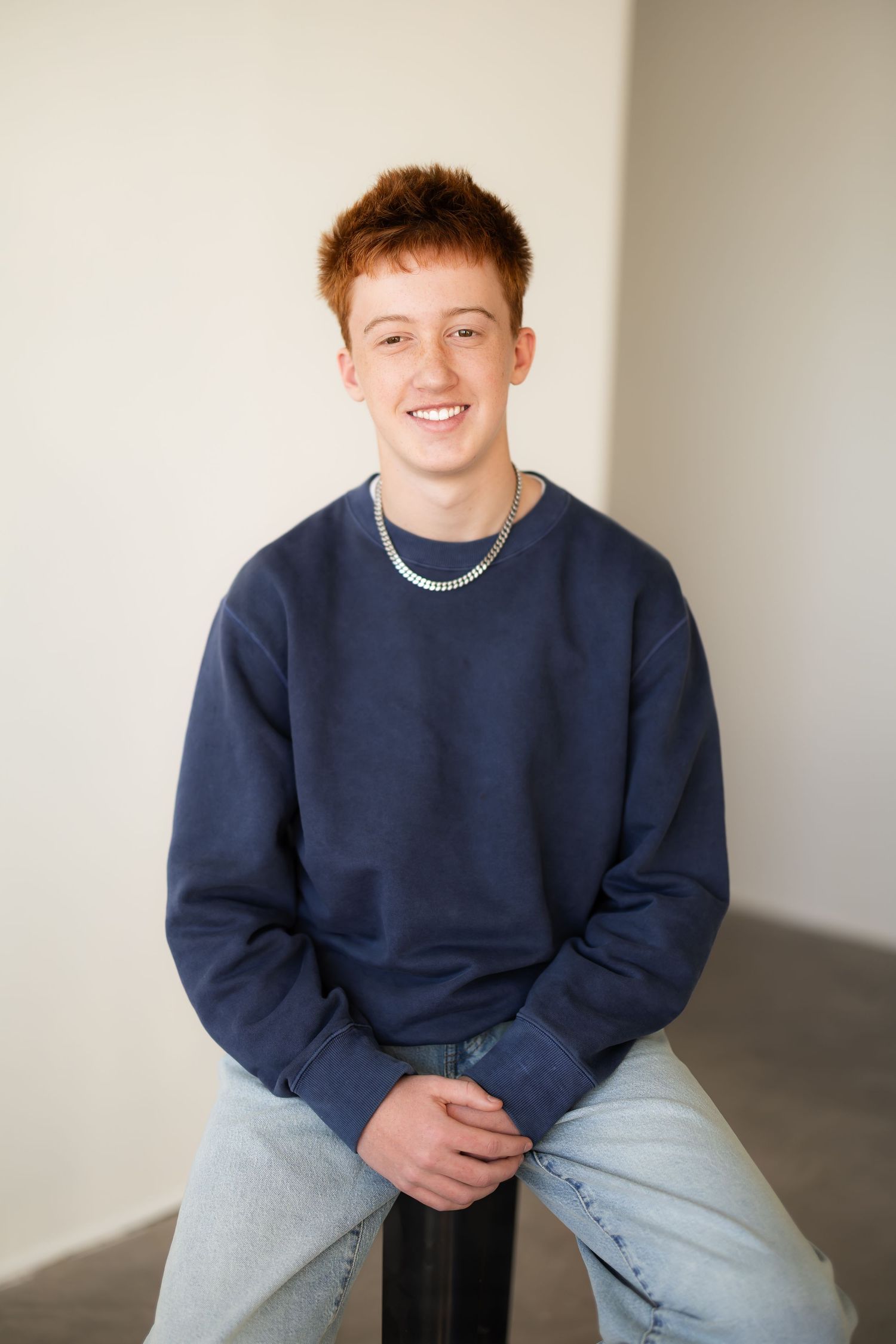 8th grade boy sits casually against neutral background.