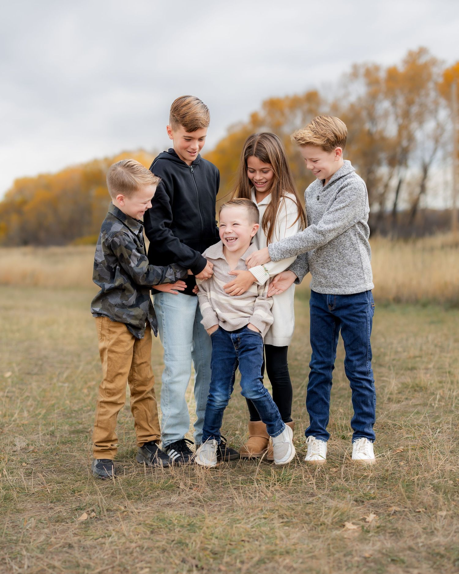 Family members playfully interact together in a golden autumn field during an outdoor photo session.