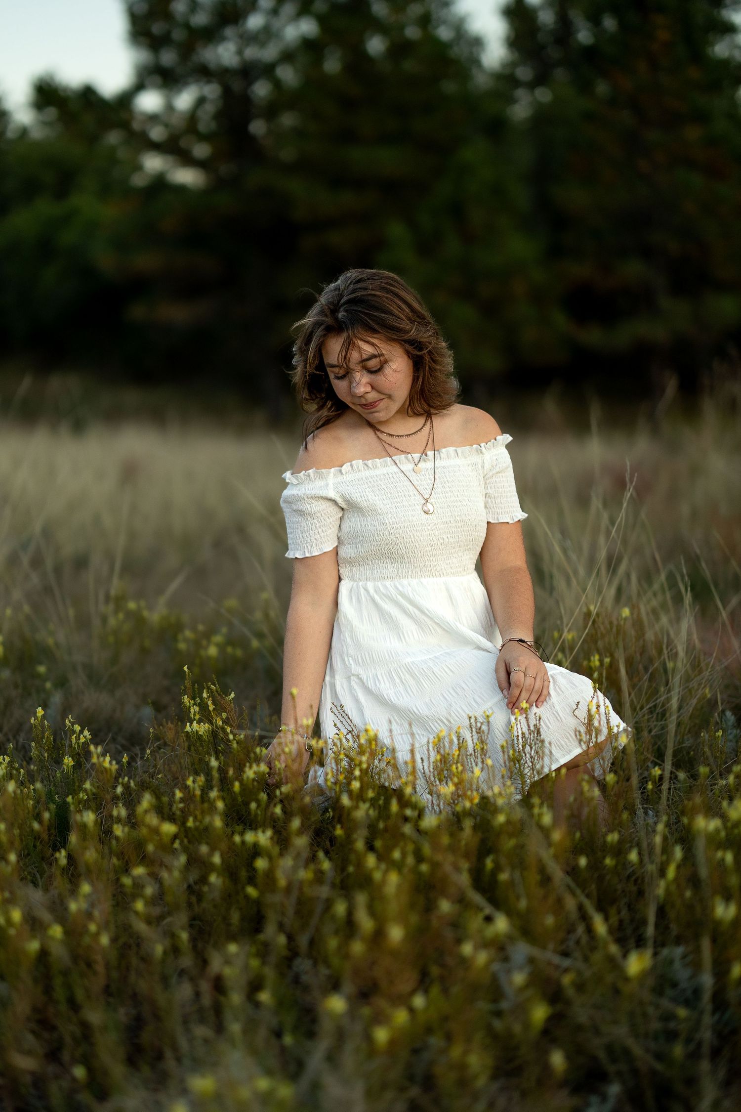 Person in white dress sitting among wildflowers in field at sunset.