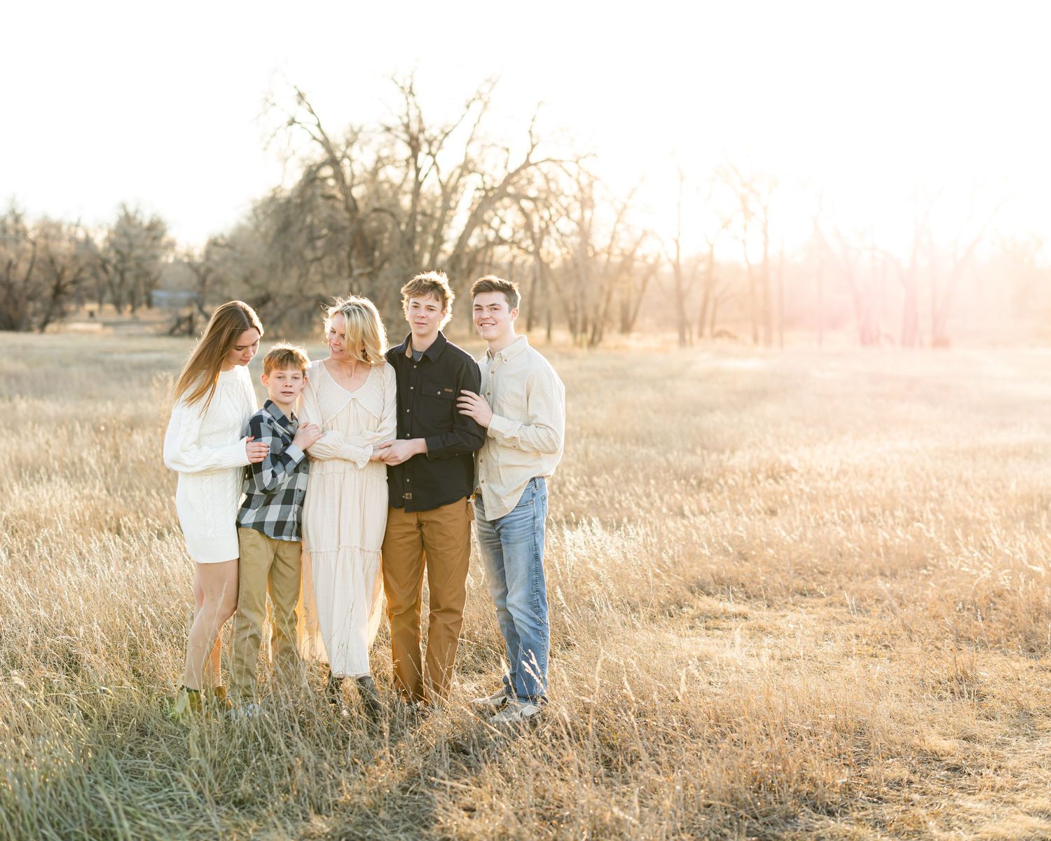 A group poses together in a golden field during sunset with trees in the background.