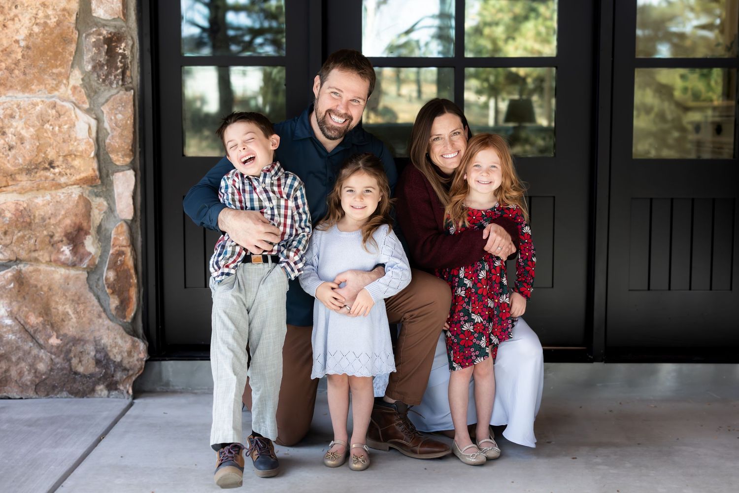 Indoor family portrait session against brick wall with black framed windows.