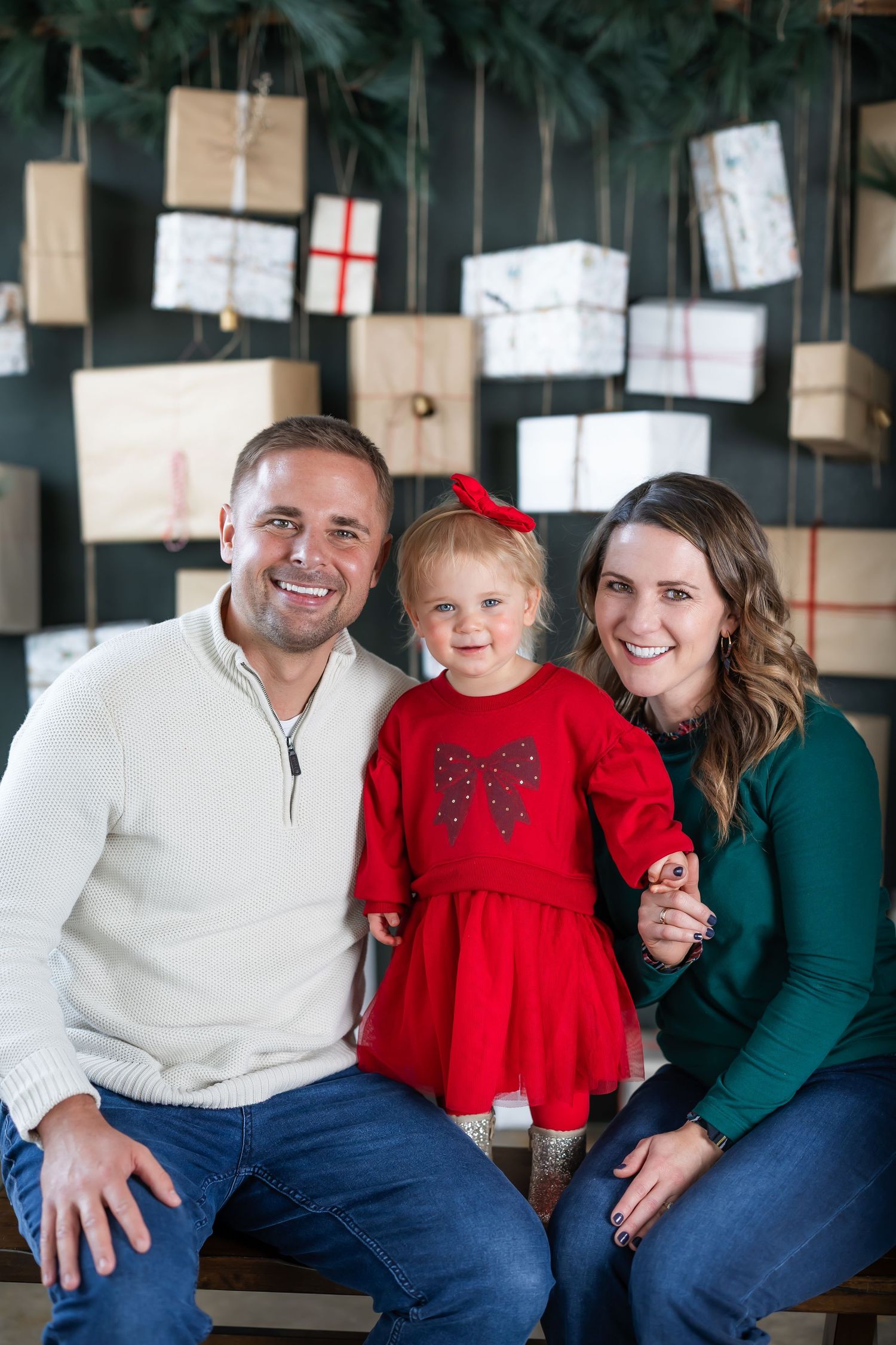Family sitting together on bench with holiday decorations and wrapped presents in background.
